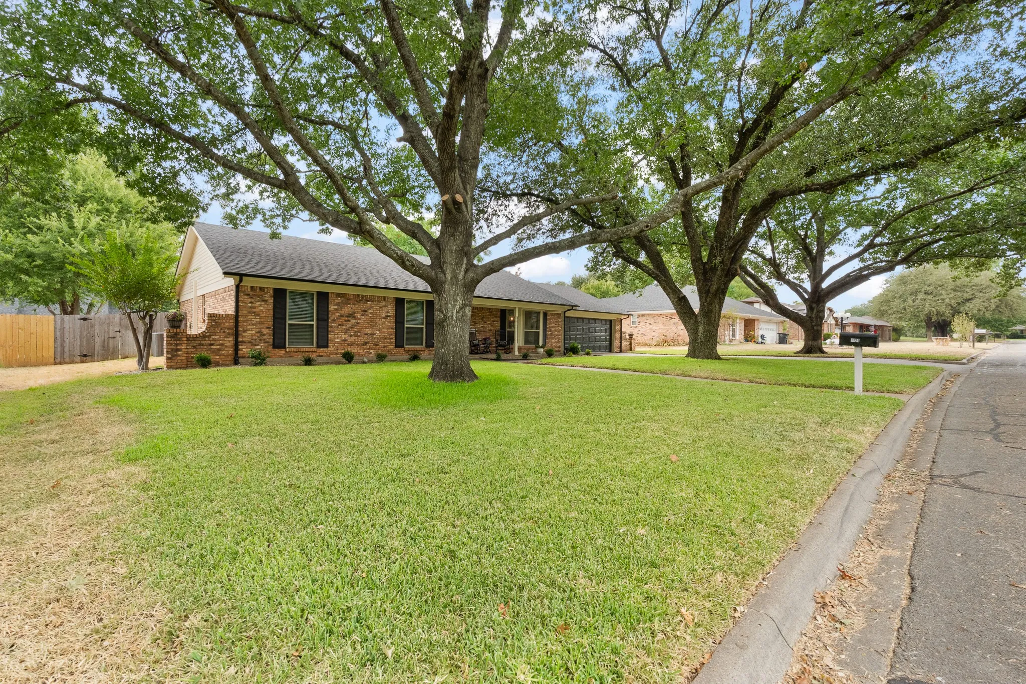 Brick exterior with a dark shingle roof, mature trees, and a manicured lawn