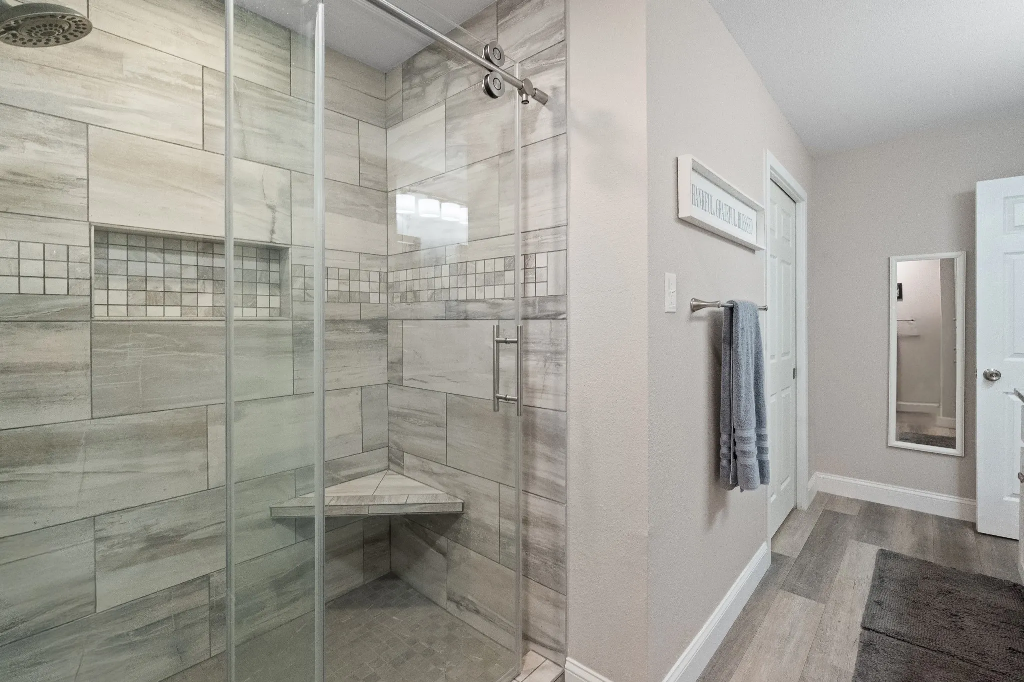 Glass-enclosed shower with a rainfall showerhead, tile-inlay niche, and corner bench