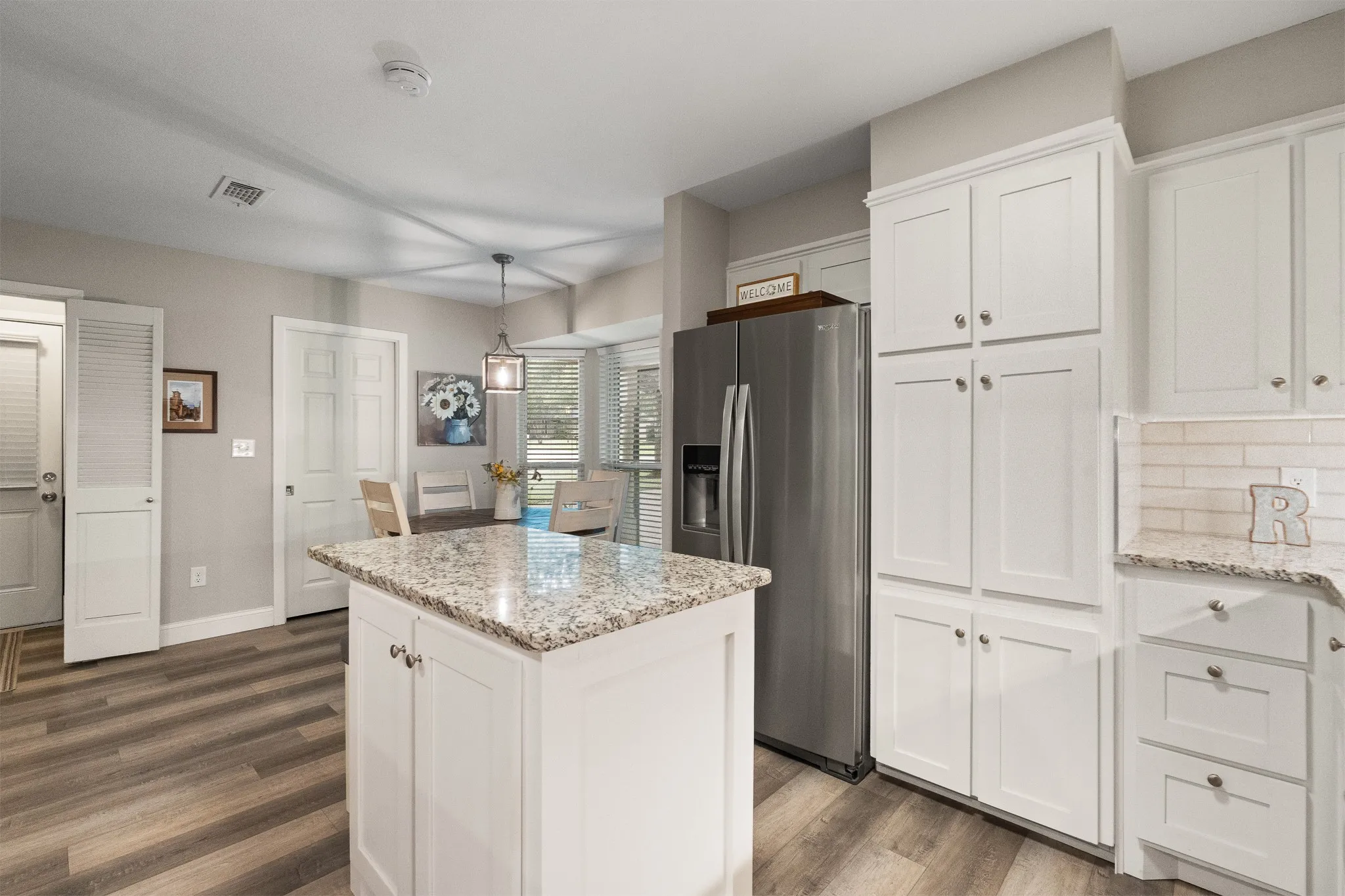 Kitchen featuring white shaker-style cabinetry, light-toned countertops, wood-finish flooring, a kitchen island, and a bay window