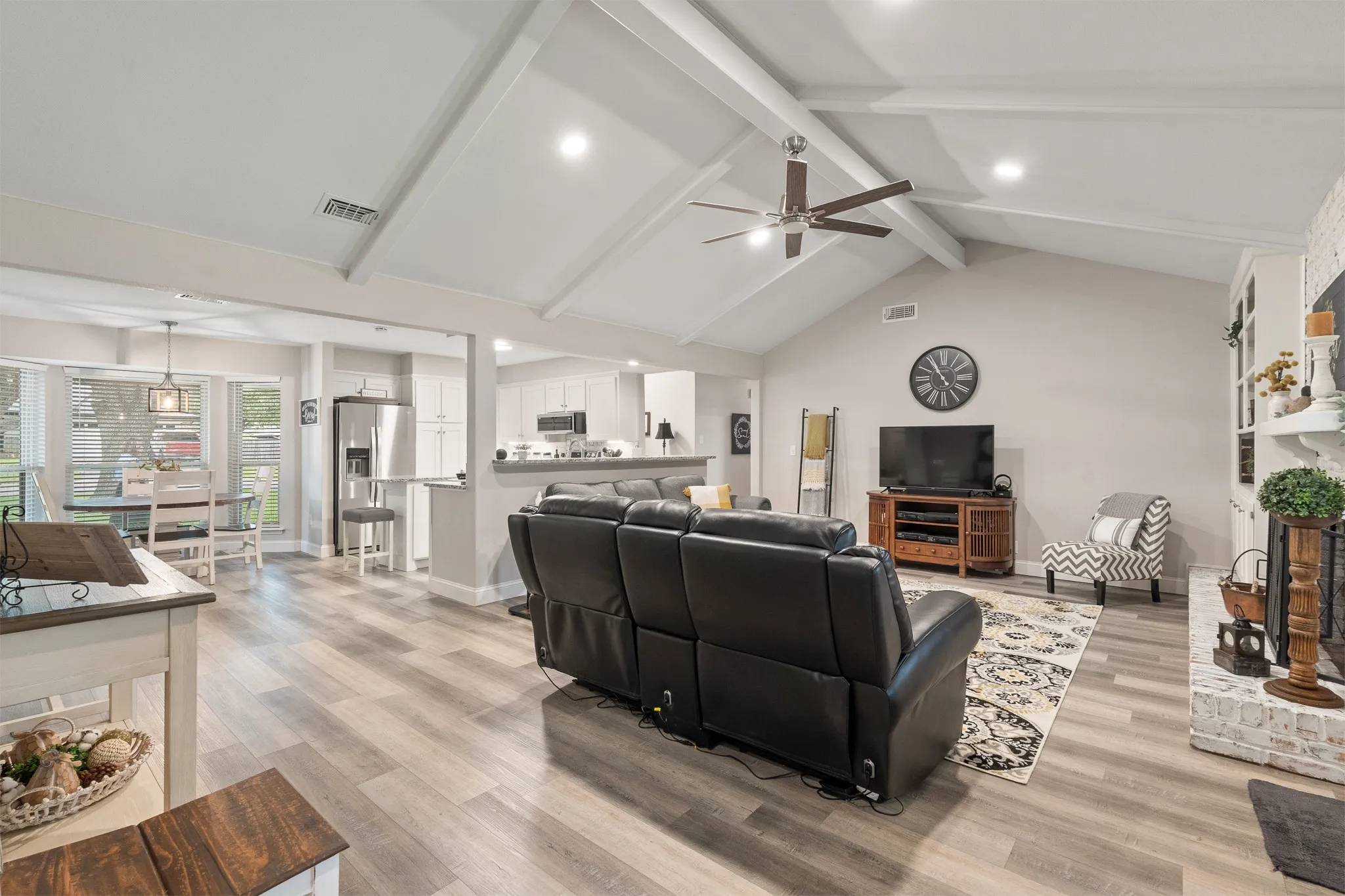 Vaulted ceiling with exposed beams, wood-finish flooring, recessed lighting, ceiling fan, and a painted brick fireplace