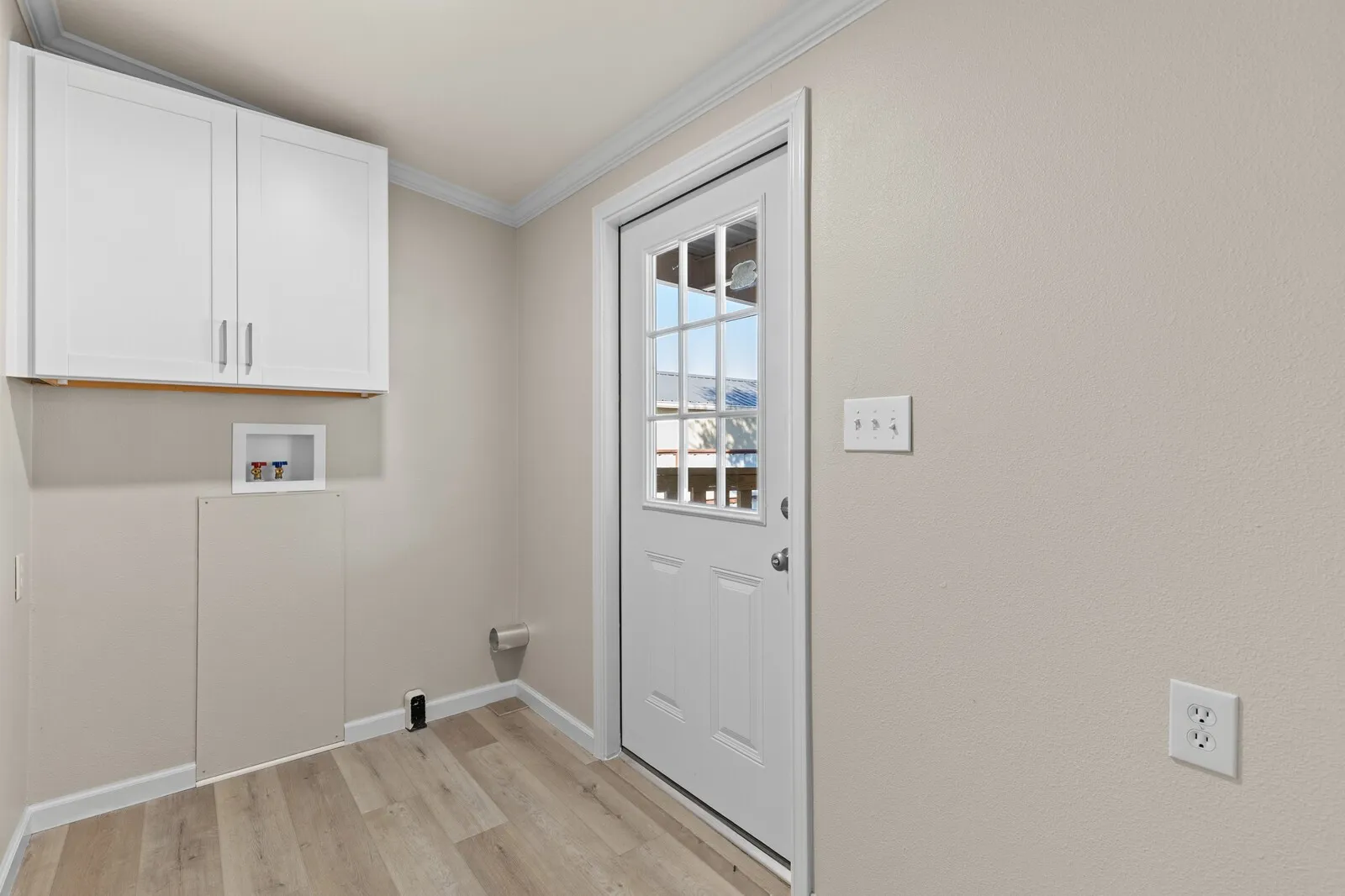 White shaker-style cabinetry, wood-finish flooring, white paneled door with glass inserts, white baseboards, and crown molding