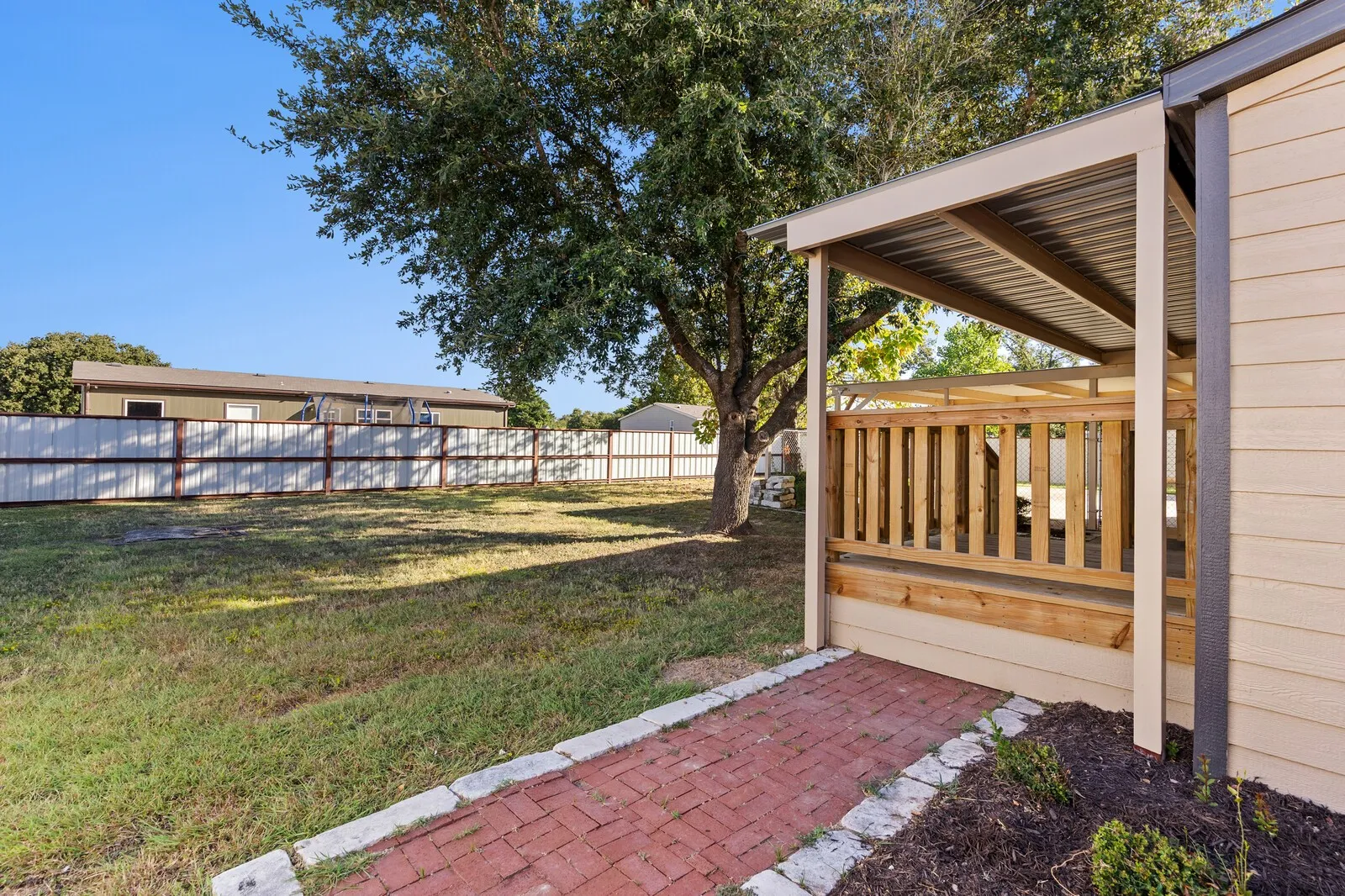 Covered outdoor patio with wood railing, corrugated metal roof, and brick pathway