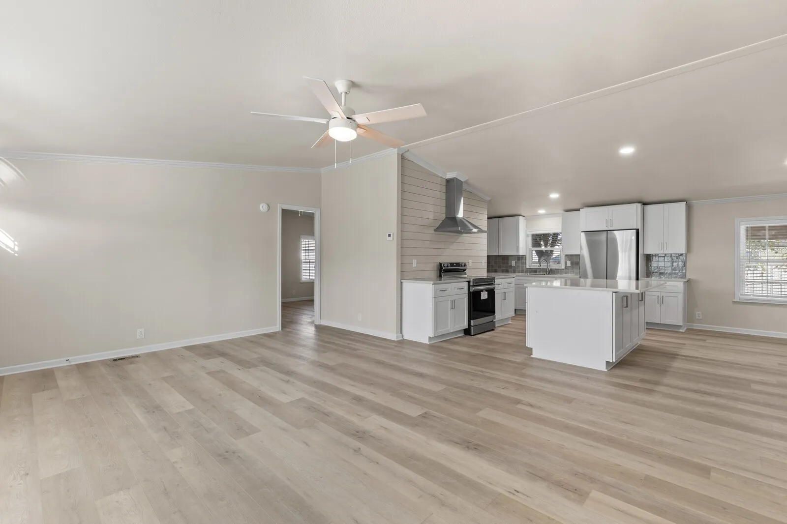 Open-concept living area with wood-finish flooring, a contemporary ceiling fan, and crown molding