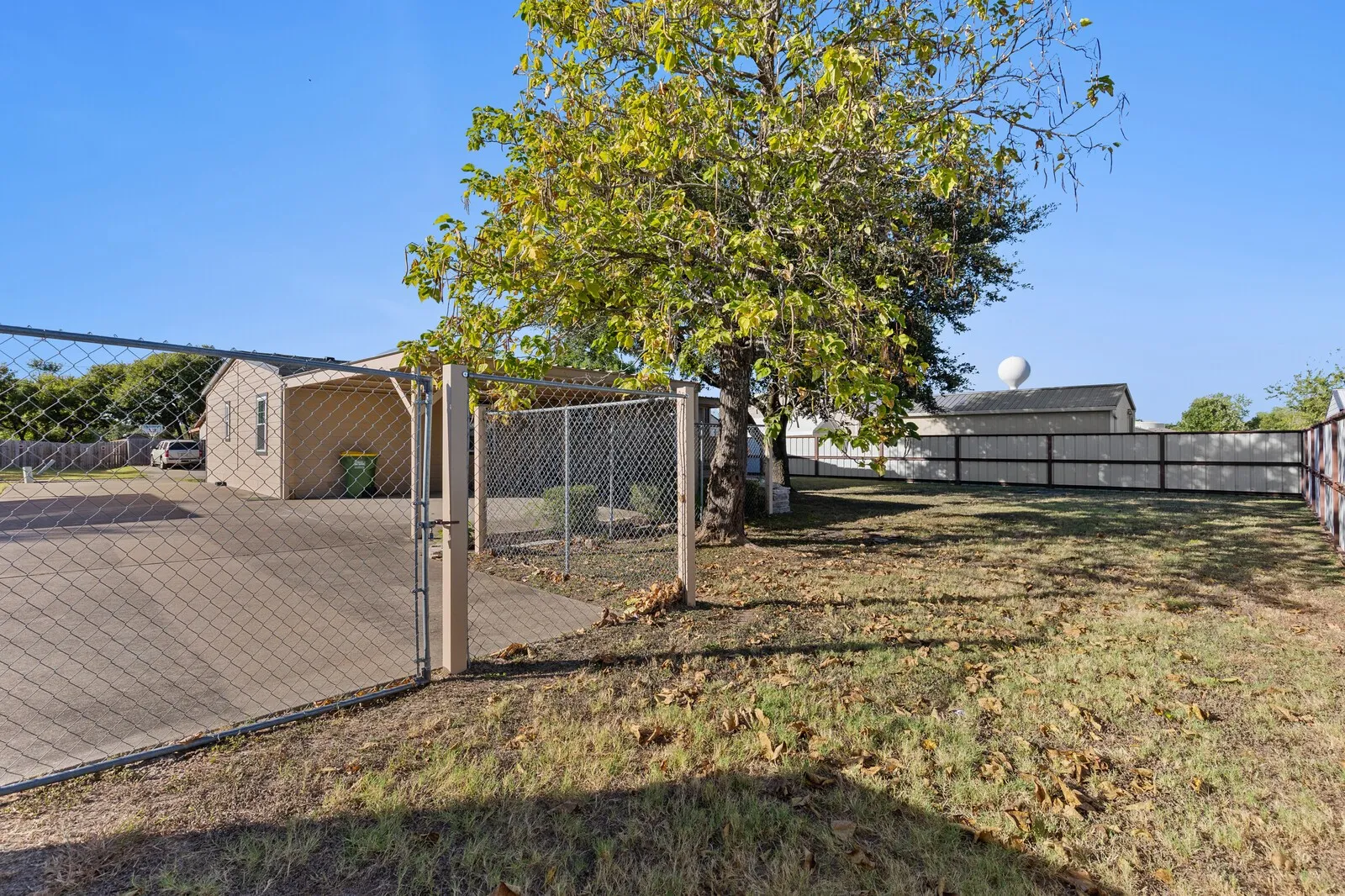 Expansive outdoor space featuring a chain-link fence, mature tree, and a concrete pad