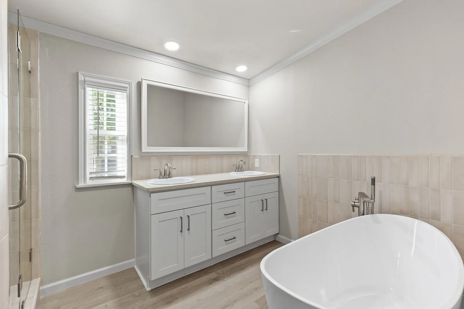 Dual sink vanity with light gray cabinetry, modern rectangular mirror, freestanding soaking tub, and a glass-enclosed shower