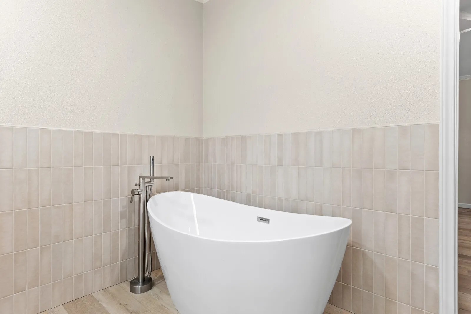 Freestanding soaking tub with a floor-mounted brushed nickel faucet, set against a tiled wall