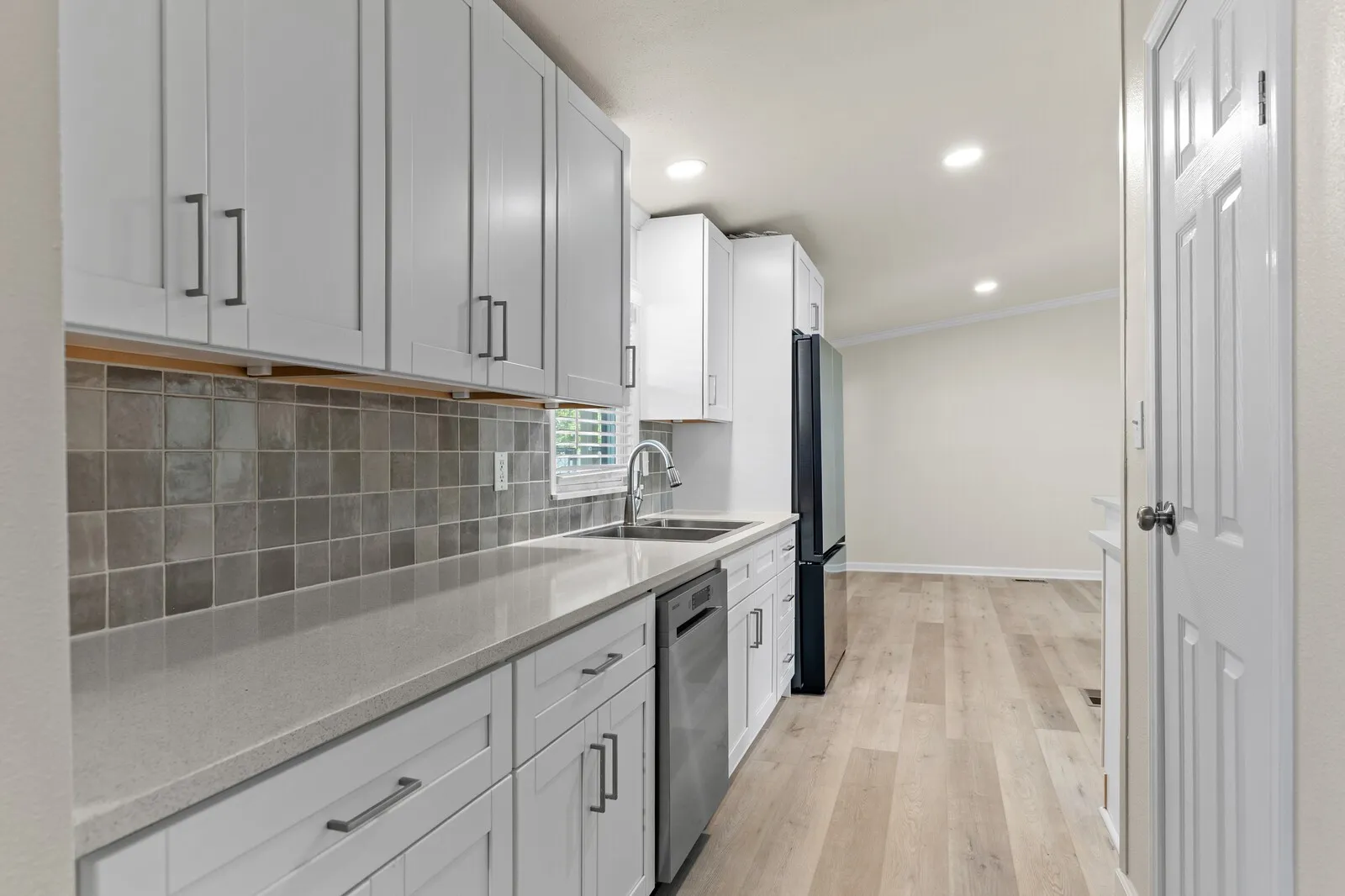 White shaker cabinetry, light-toned countertops, subway tile backsplash, stainless steel sink with a gooseneck faucet, and light wood-finish flooring