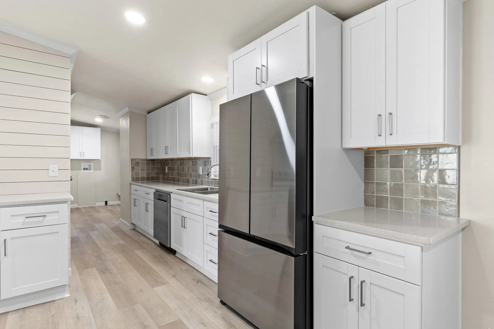 Kitchen featuring white shaker cabinetry, stainless steel appliances, light wood-finish flooring, and a tiled backsplash