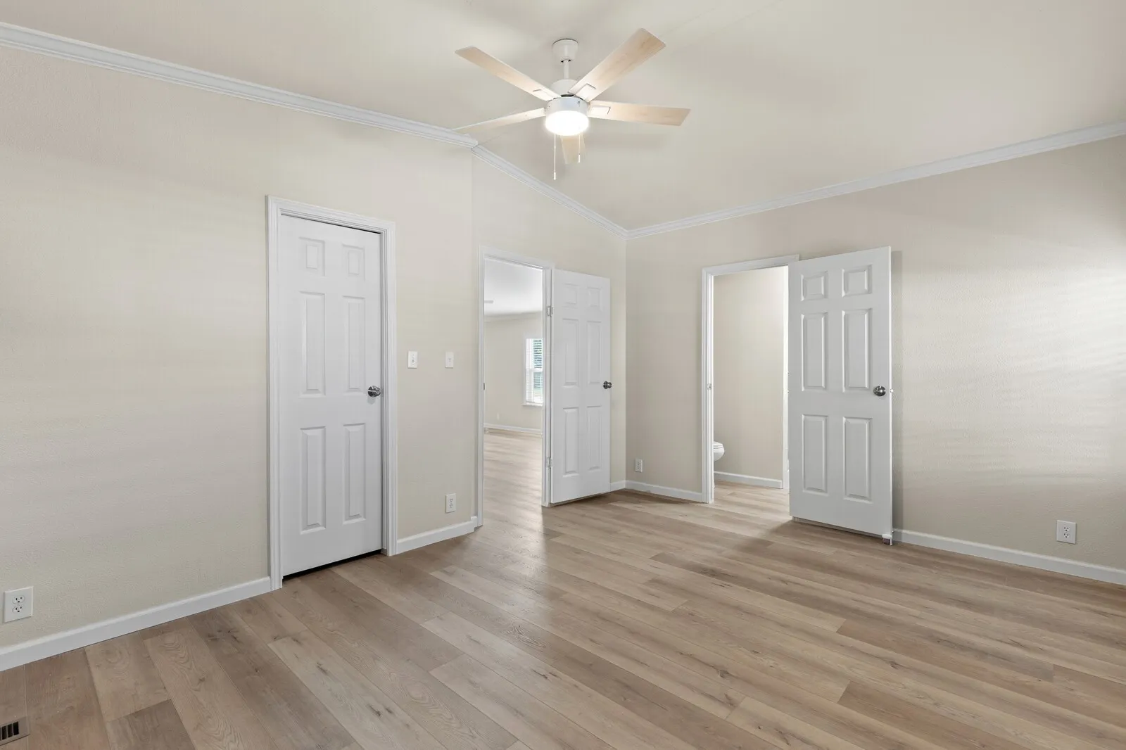 Vaulted ceiling with crown molding, wood-finish flooring, and a ceiling fan with integrated lighting