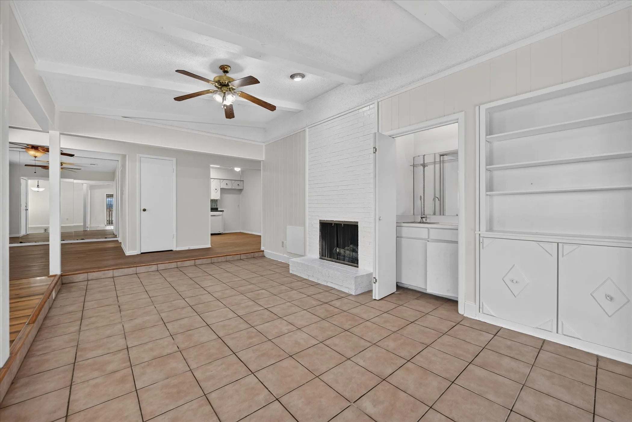 Tiled flooring, exposed ceiling beams, a white brick fireplace, and built-in shelving