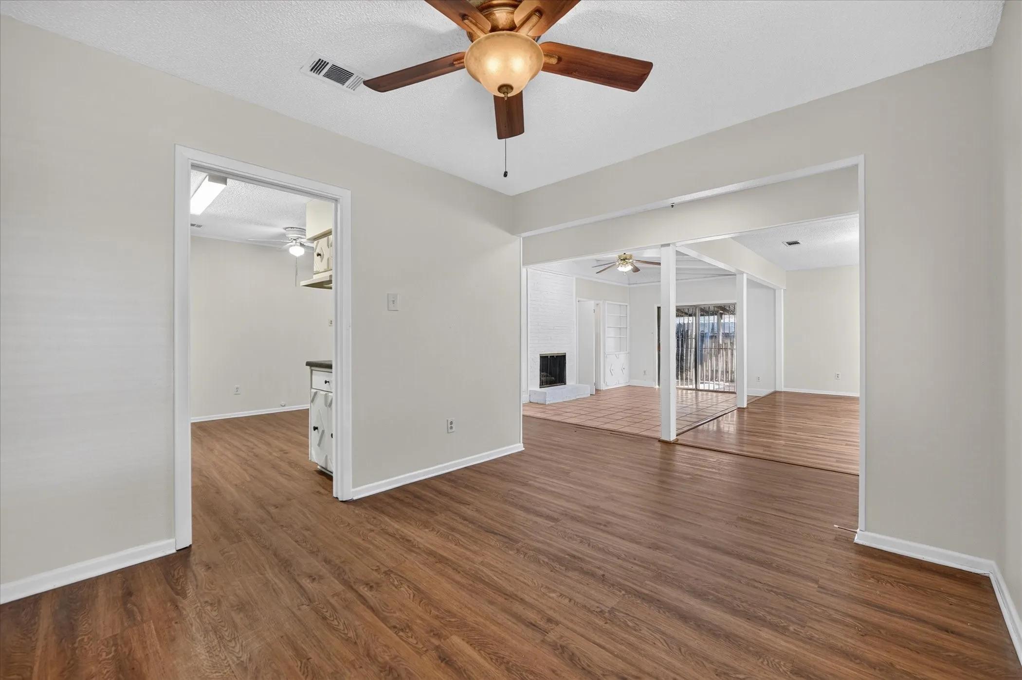 Wood-finish flooring throughout, light neutral wall paint, and a wood-bladed ceiling fan