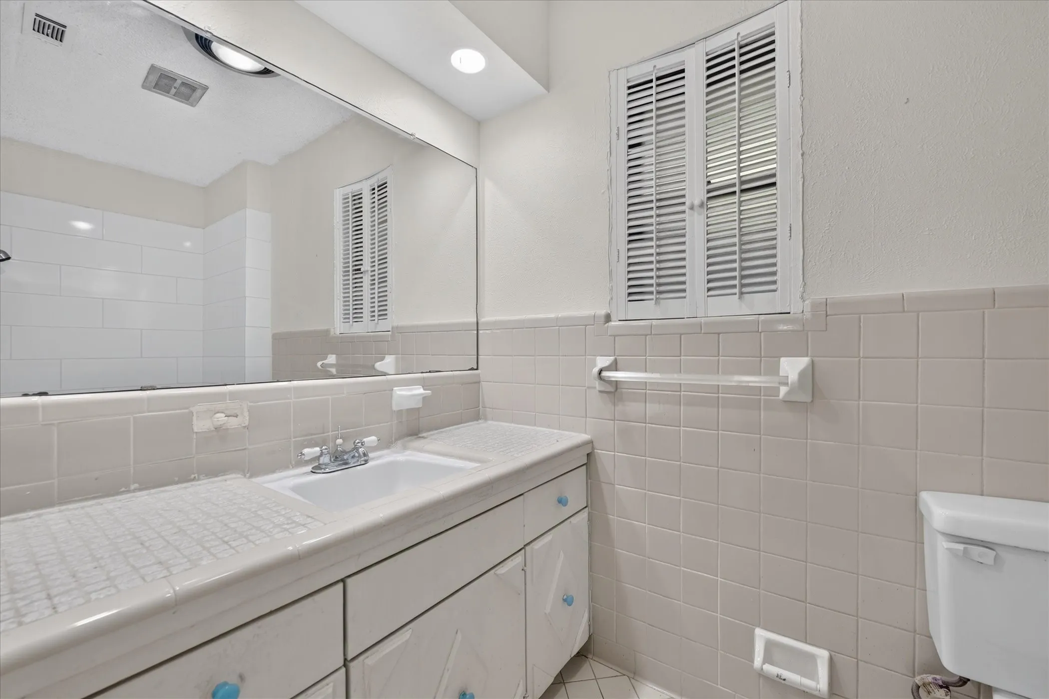 Bathroom featuring a vanity with an integrated sink, a large wall mirror, and tile wainscoting