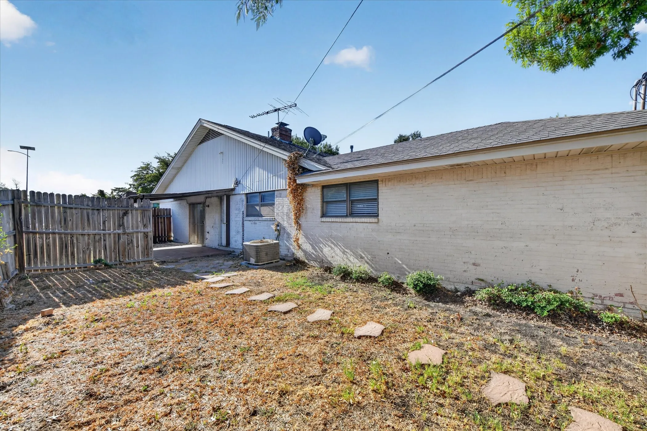Backyard area with a wood fence, concrete patio, and stepping stones