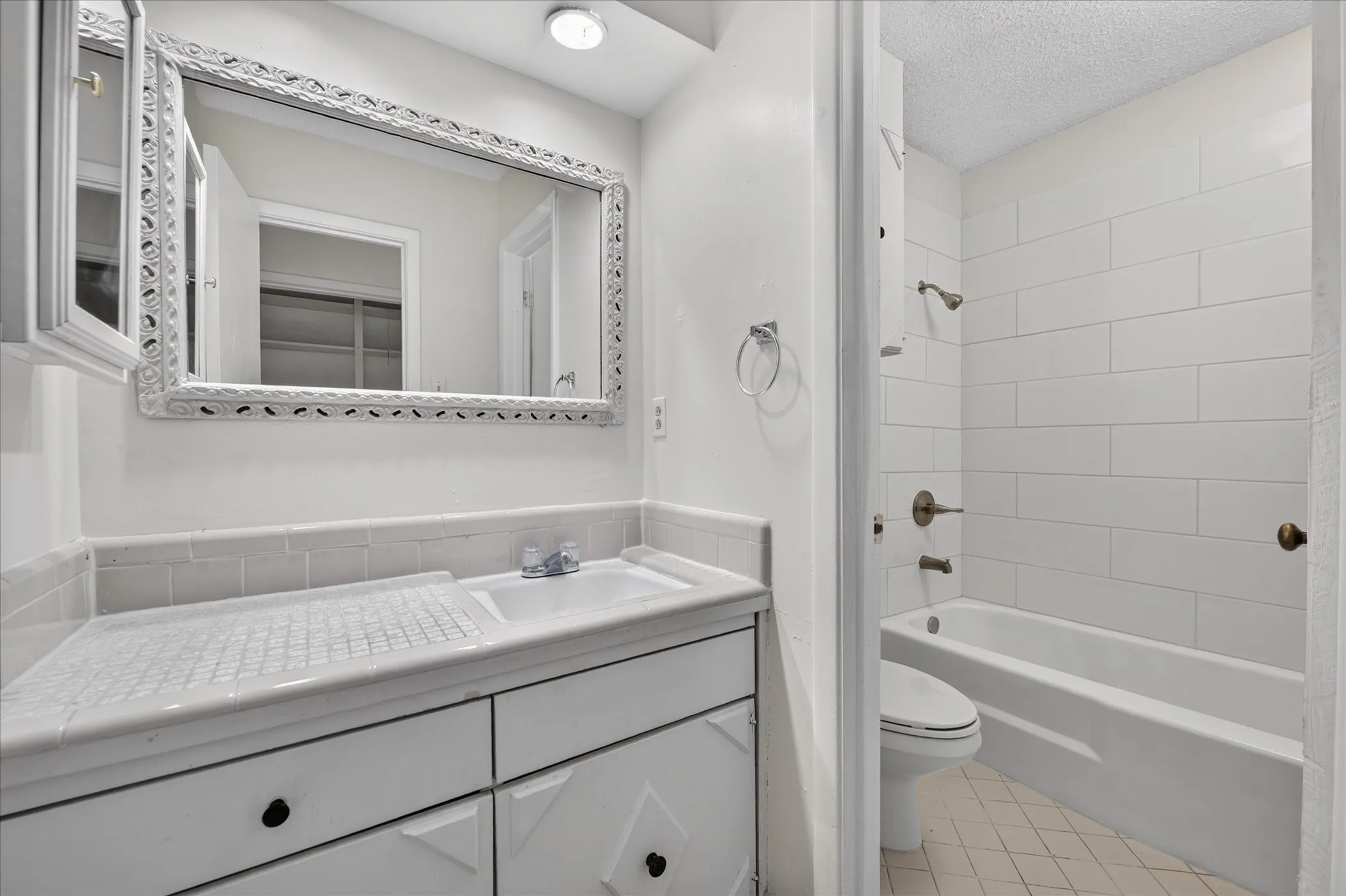 Vanity with integrated sink and storage, decorative framed mirror, recessed lighting, and a bathtub with subway tile surround