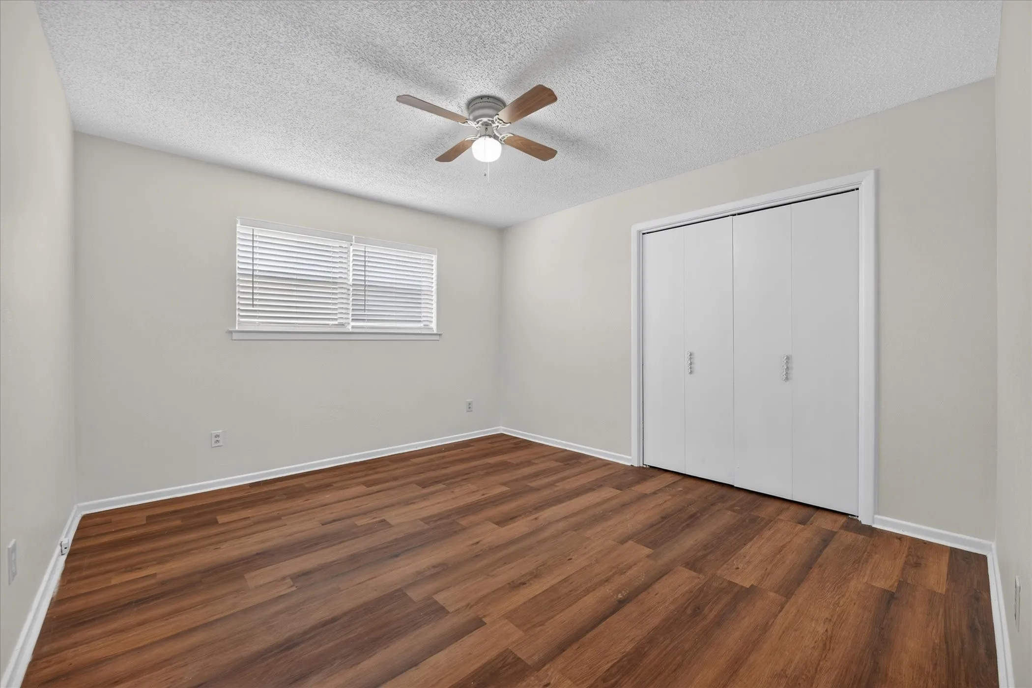 Neutral wall tones, wood-finish flooring, window with blinds, bi-fold closet doors, and a ceiling fan with integrated lighting