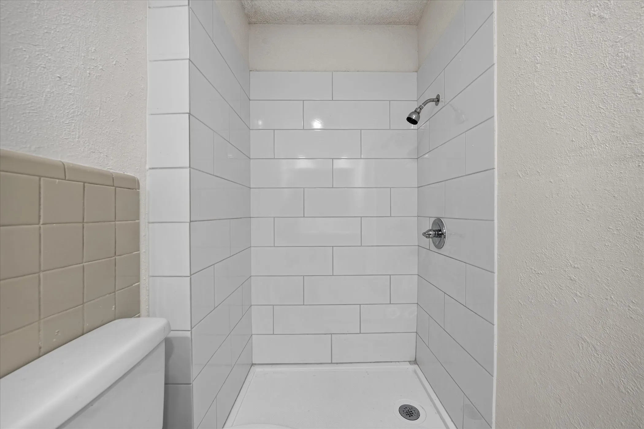 Shower stall with white subway tile surround, chrome shower head, and chrome faucet hardware