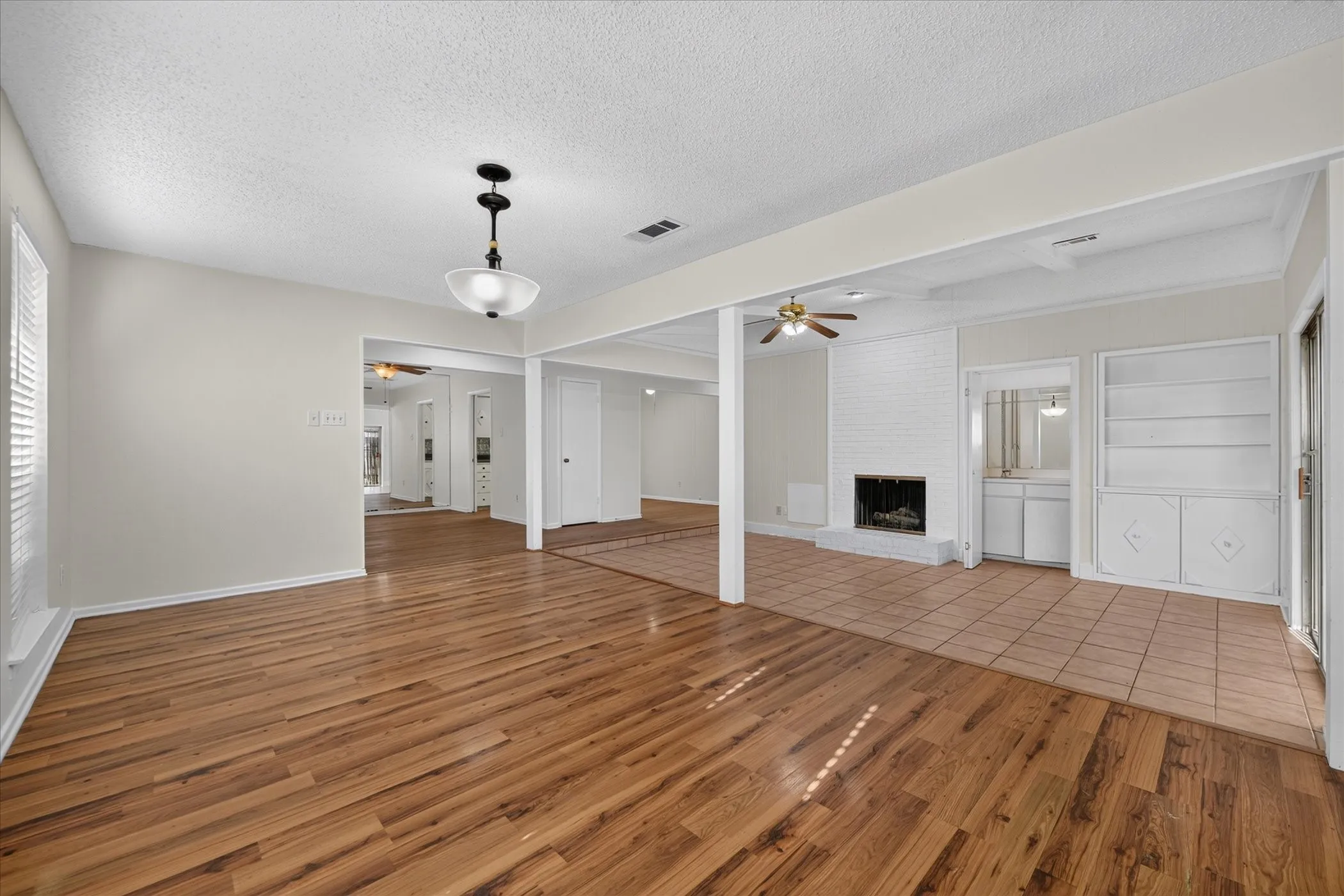 Wood-finish flooring, recessed lighting, white brick fireplace, built-in shelving, and tile flooring