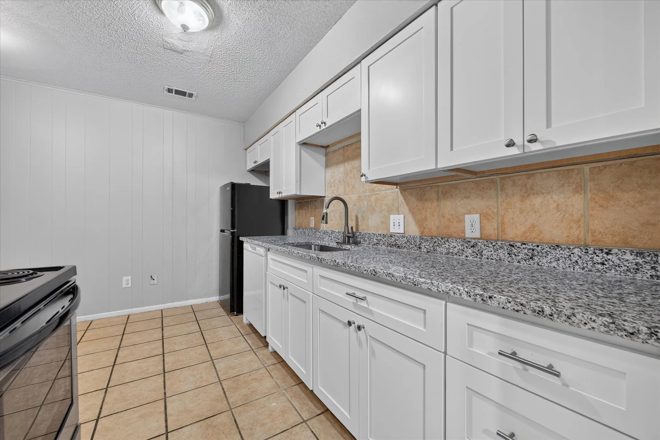 Kitchen featuring white shaker cabinetry, speckled countertops, a tile backsplash, and tile flooring