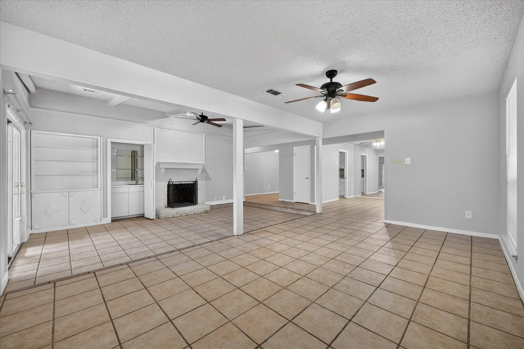 Spacious living area featuring tile flooring, a fireplace with a brick surround, and built-in shelving with a wet bar