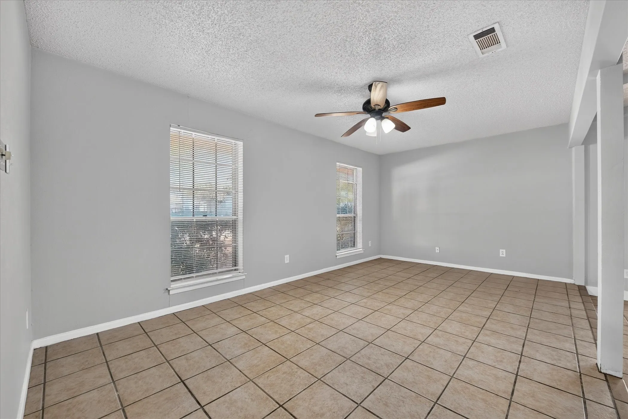 Spacious room featuring tile flooring, neutral wall tones, multiple windows, and a ceiling fan with integrated lighting