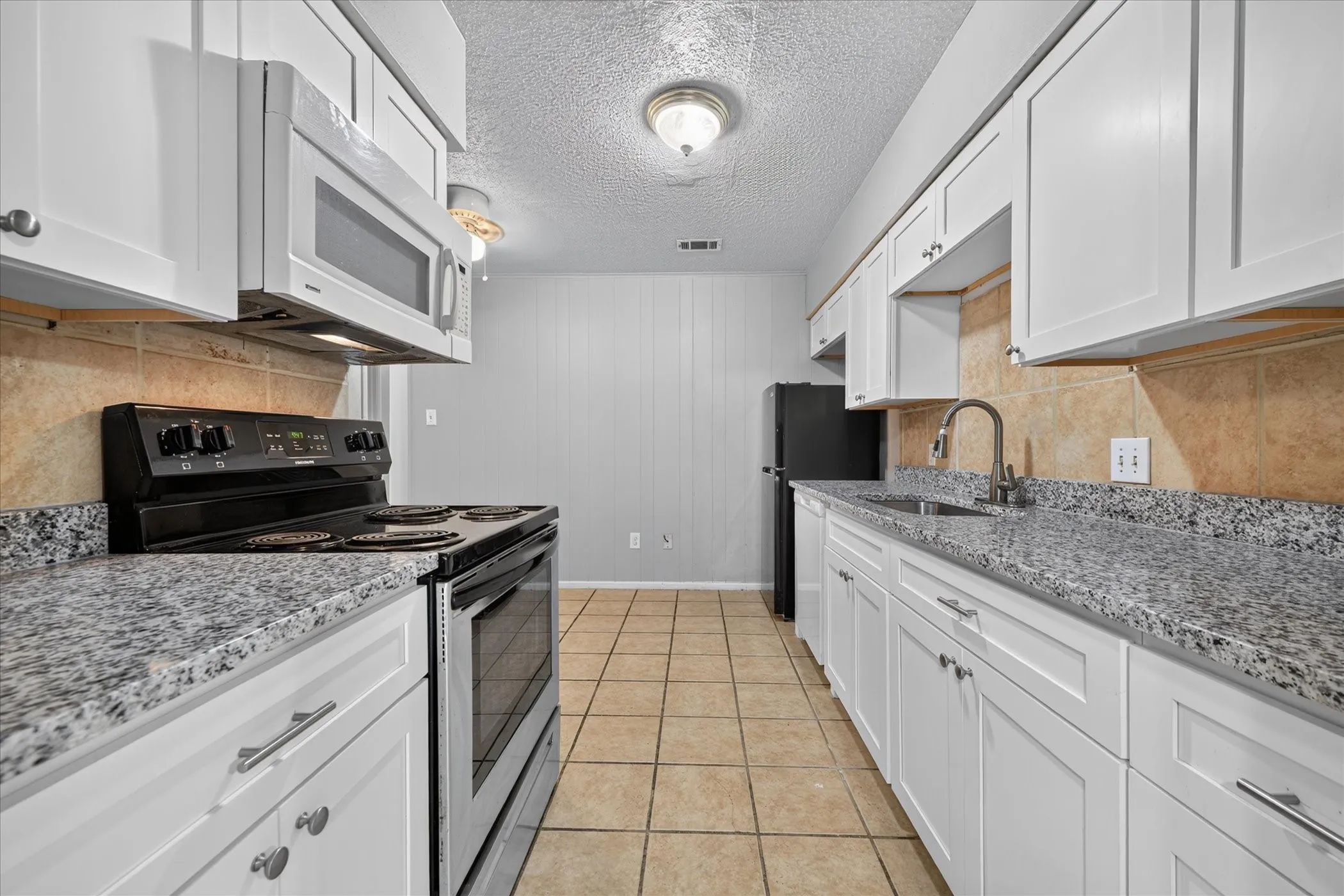 Galley kitchen featuring white cabinetry, speckled countertops, stainless steel appliances, and tile flooring