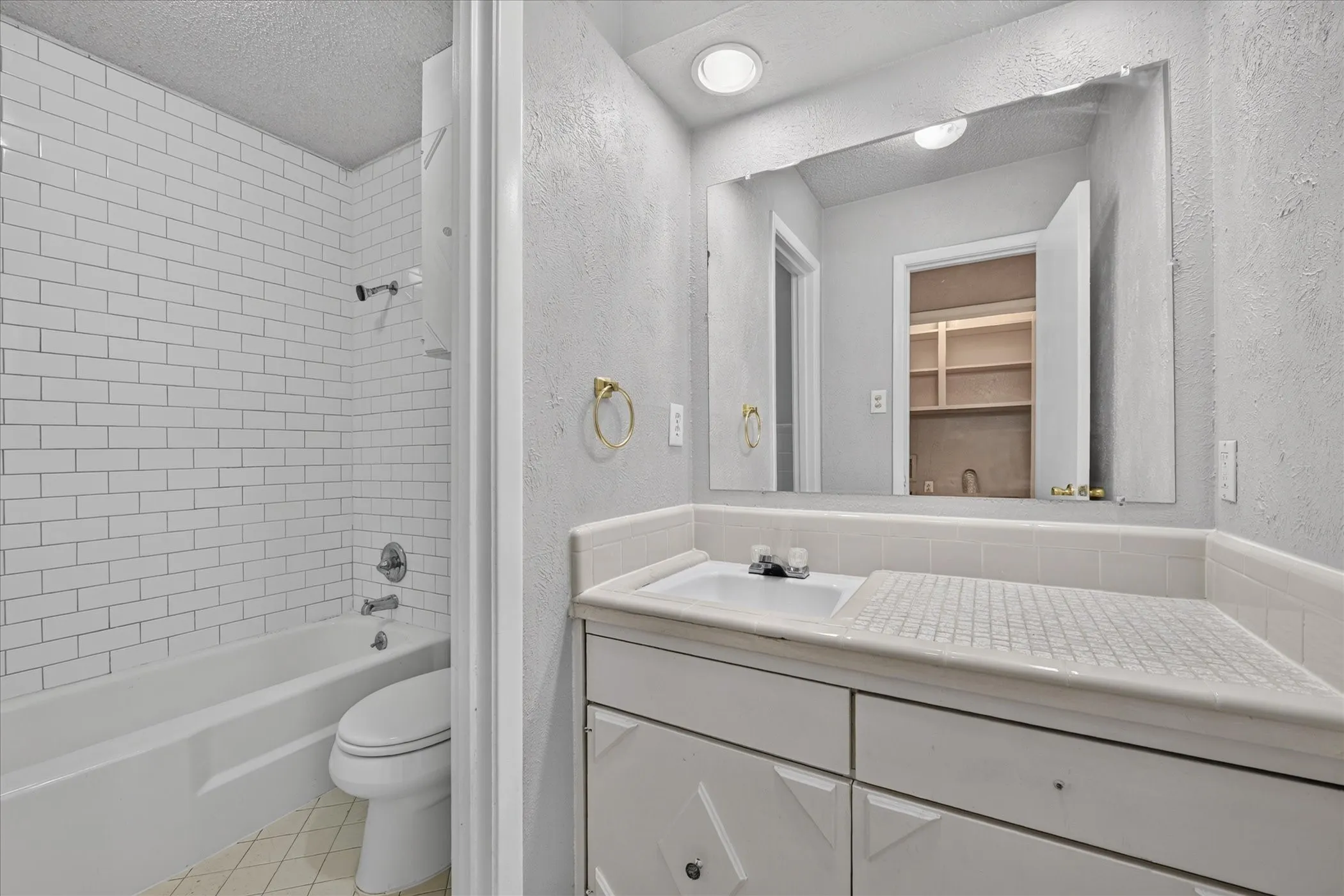 Tub and shower combination with subway tile surround, single vanity with integrated sink, and built-in storage shelves