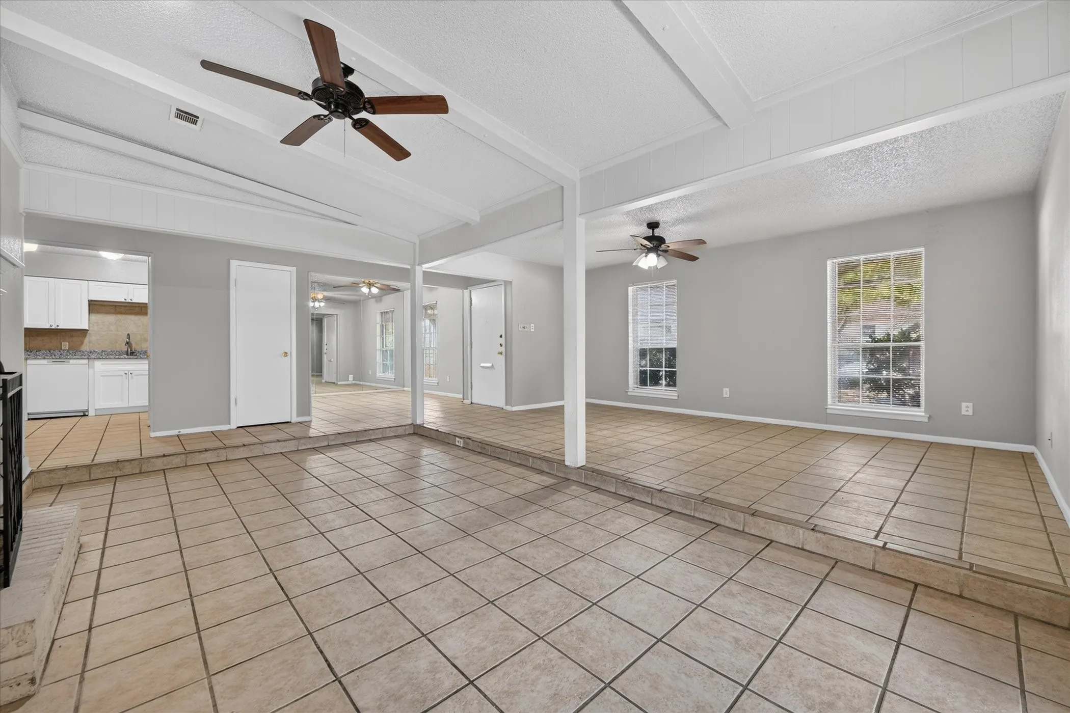 Spacious living area featuring tile flooring, neutral wall tones, multiple windows, and exposed ceiling beams