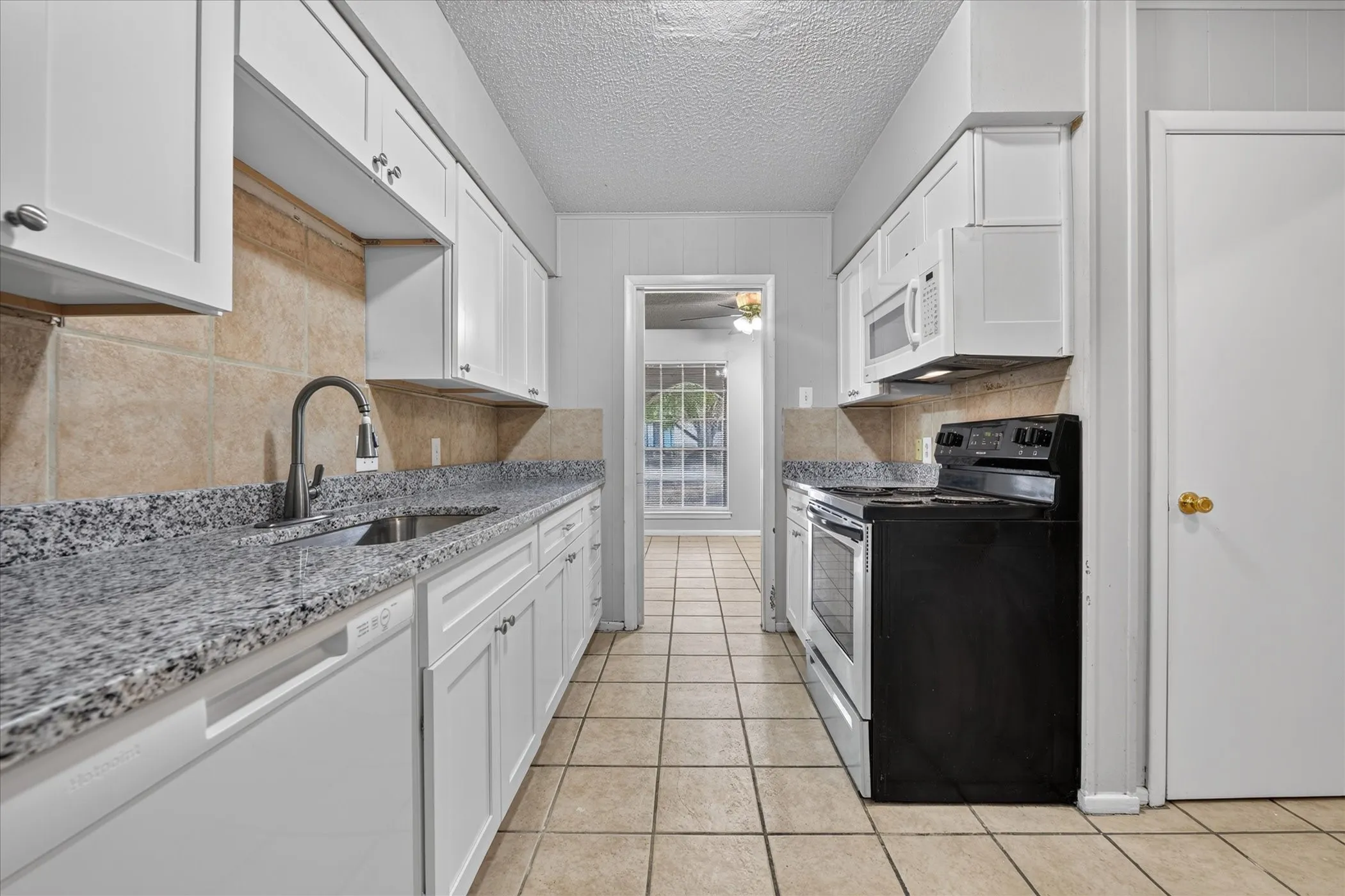 Kitchen with white cabinetry, light-toned tile flooring, and gray speckled countertops