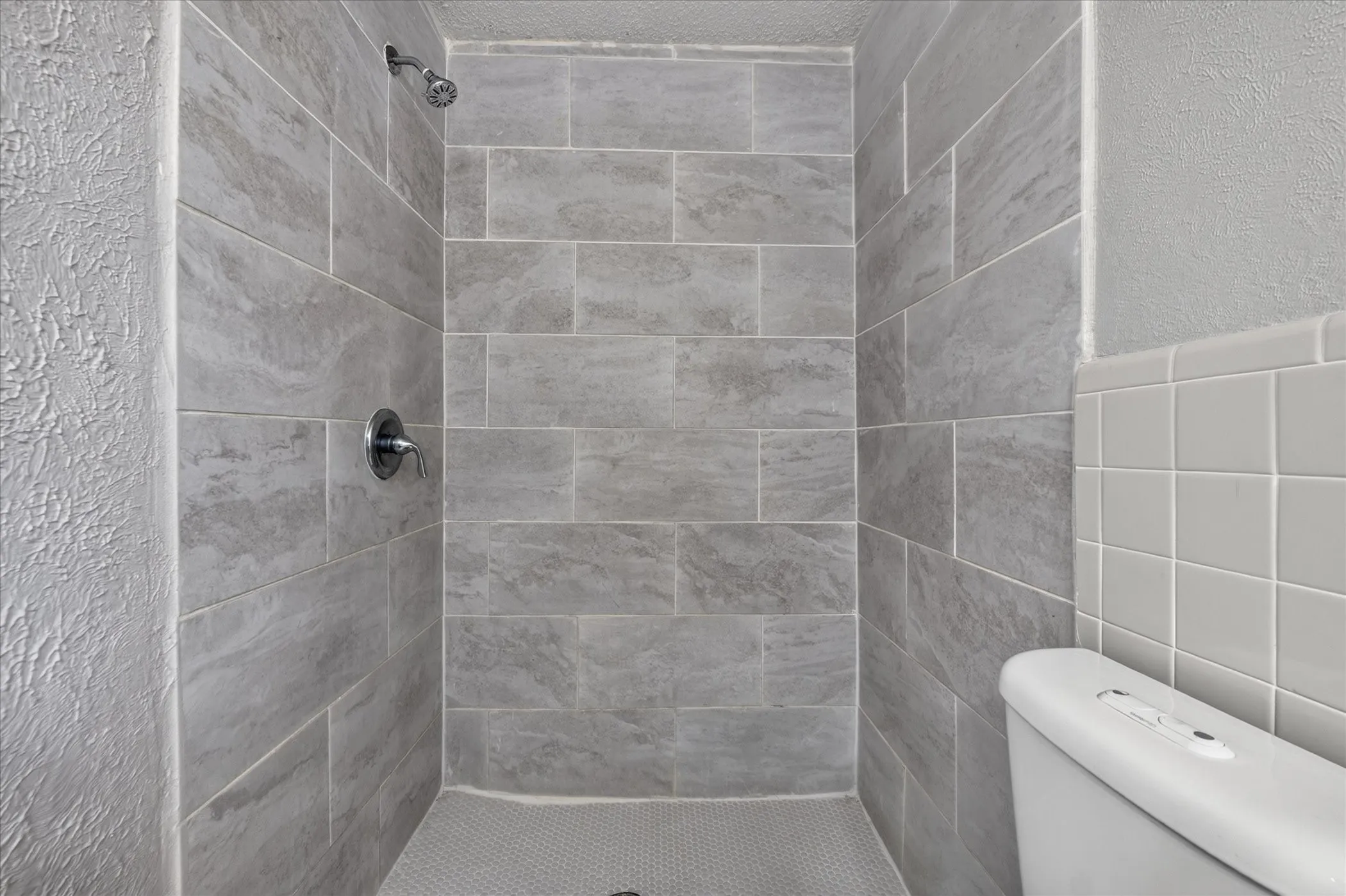 Shower with large format gray tile surround, chrome shower fixture, and hexagonal tile flooring