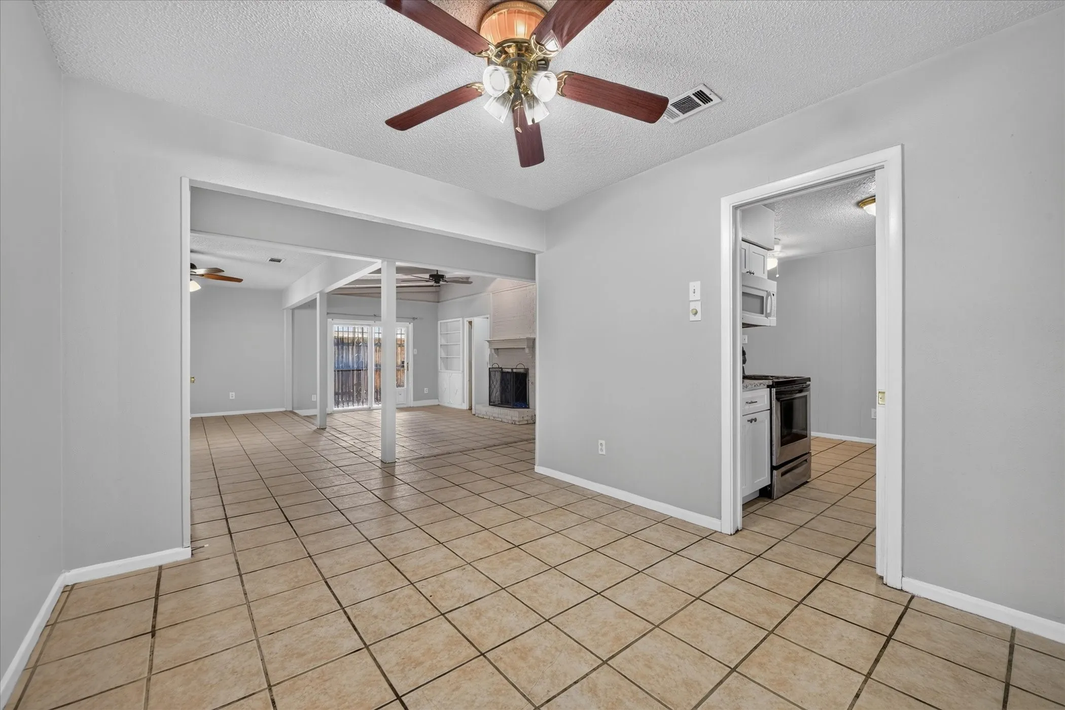 Tile flooring throughout, neutral gray wall tones, ceiling fan, and stainless steel kitchen appliances