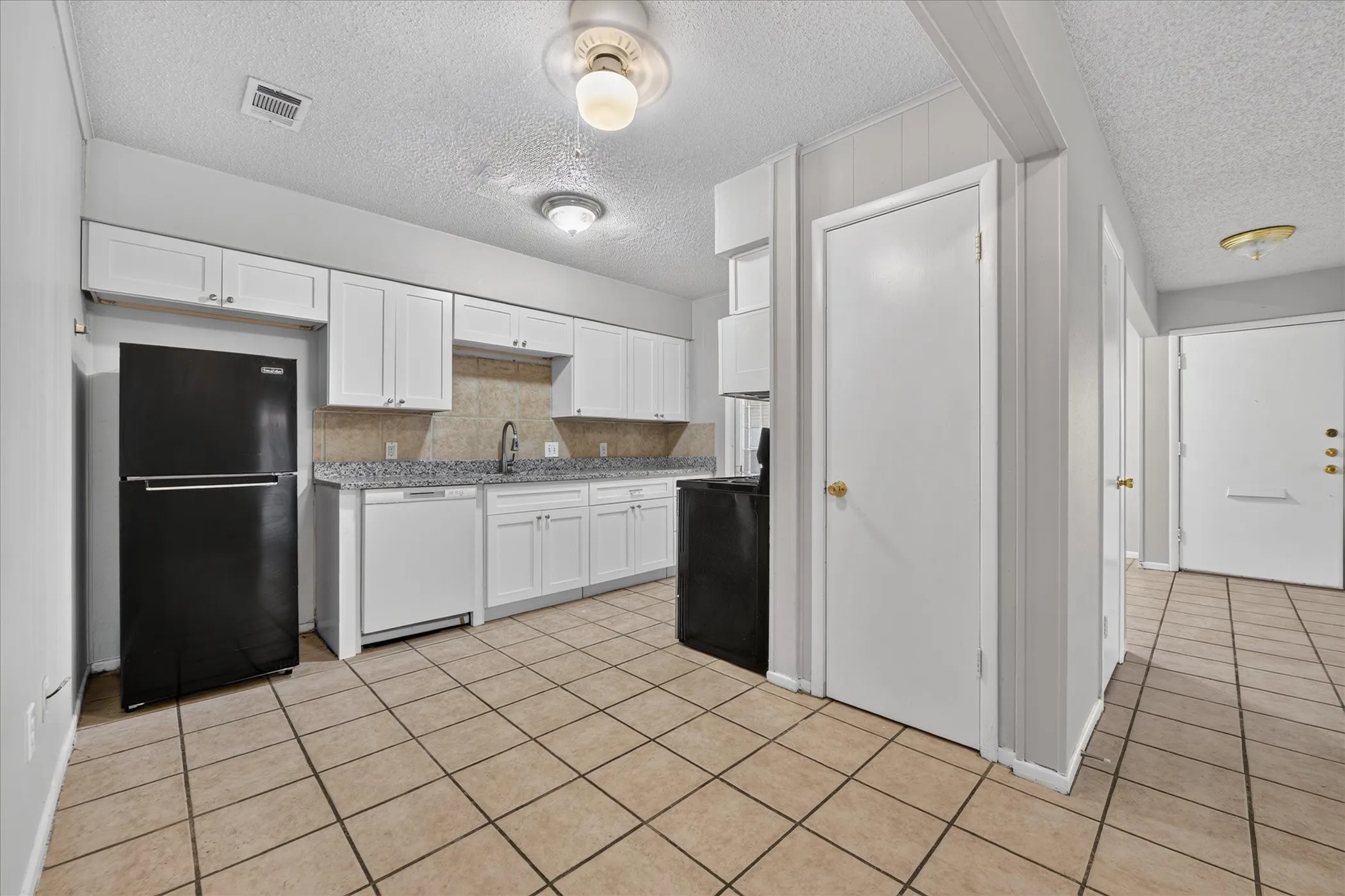 Kitchen featuring white cabinetry, light-toned tile flooring, and speckled countertops