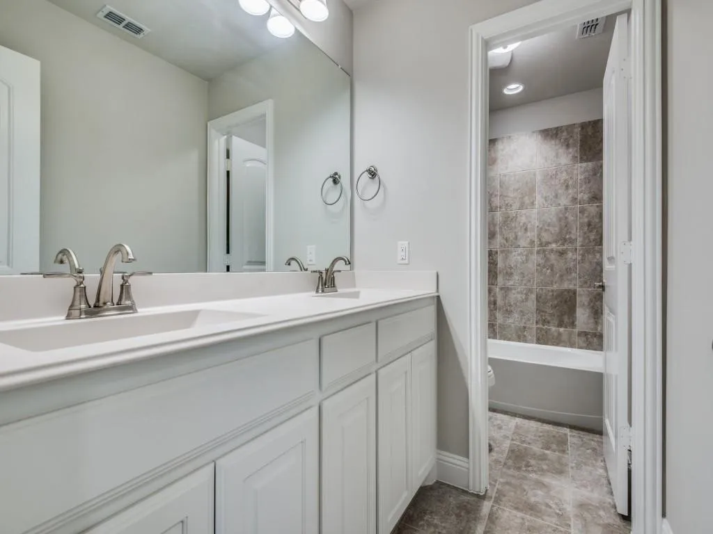 Dual vanity with integrated sinks, white cabinetry, brushed nickel fixtures, and a spacious mirror