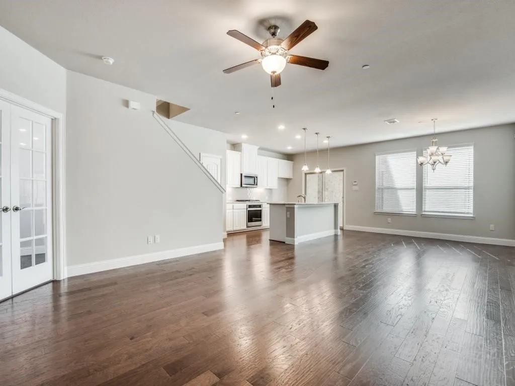 Open-concept living area with dark wood-finish flooring, white cabinetry, a kitchen island with pendant lighting, and multiple windows