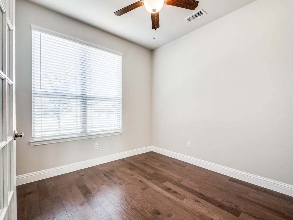 Wood-finish flooring, ceiling fan with integrated lighting, large window with blinds, and a French door entry