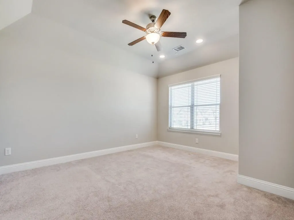 Spacious bedroom with neutral wall finishes, plush carpeting, and abundant natural light from a large double-hung window with plantation shutters