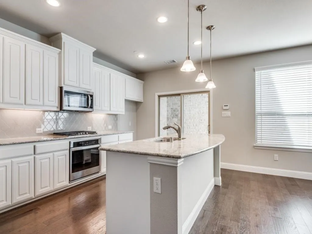 White cabinetry, stainless steel appliances, granite countertops, tile backsplash, and wood-finish flooring