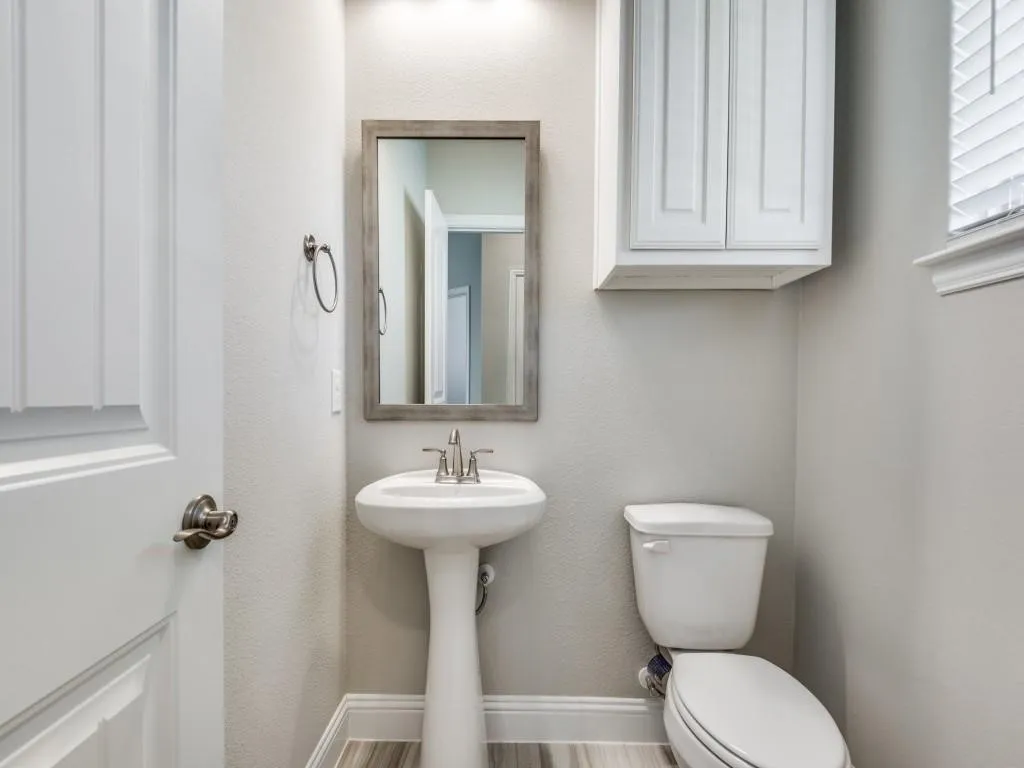 Half Bath with Pedestal sink with brushed nickel faucet, framed mirror, and wall-mounted cabinetry