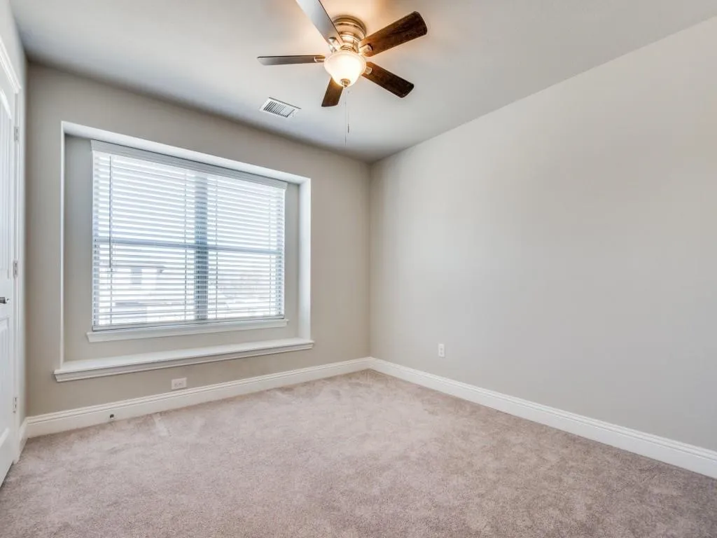 Bright secondary bedroom with plush carpeting, generous natural light from dual-pane windows with plantation shutters, and ceiling fan with integrated lighting