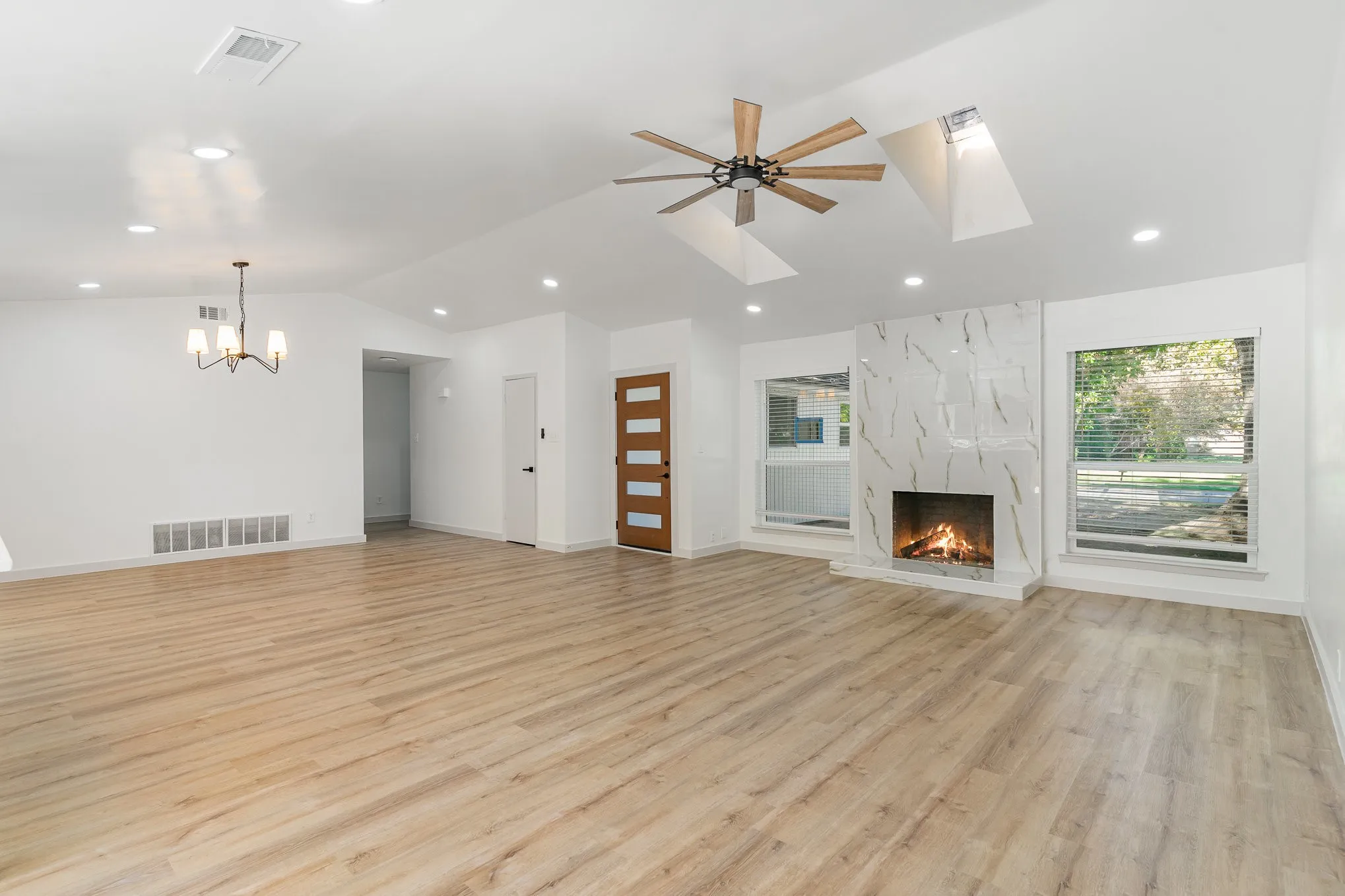Unfurnished living room featuring ceiling fan with notable chandelier, light hardwood / wood-style floors, vaulted ceiling, and a premium fireplace