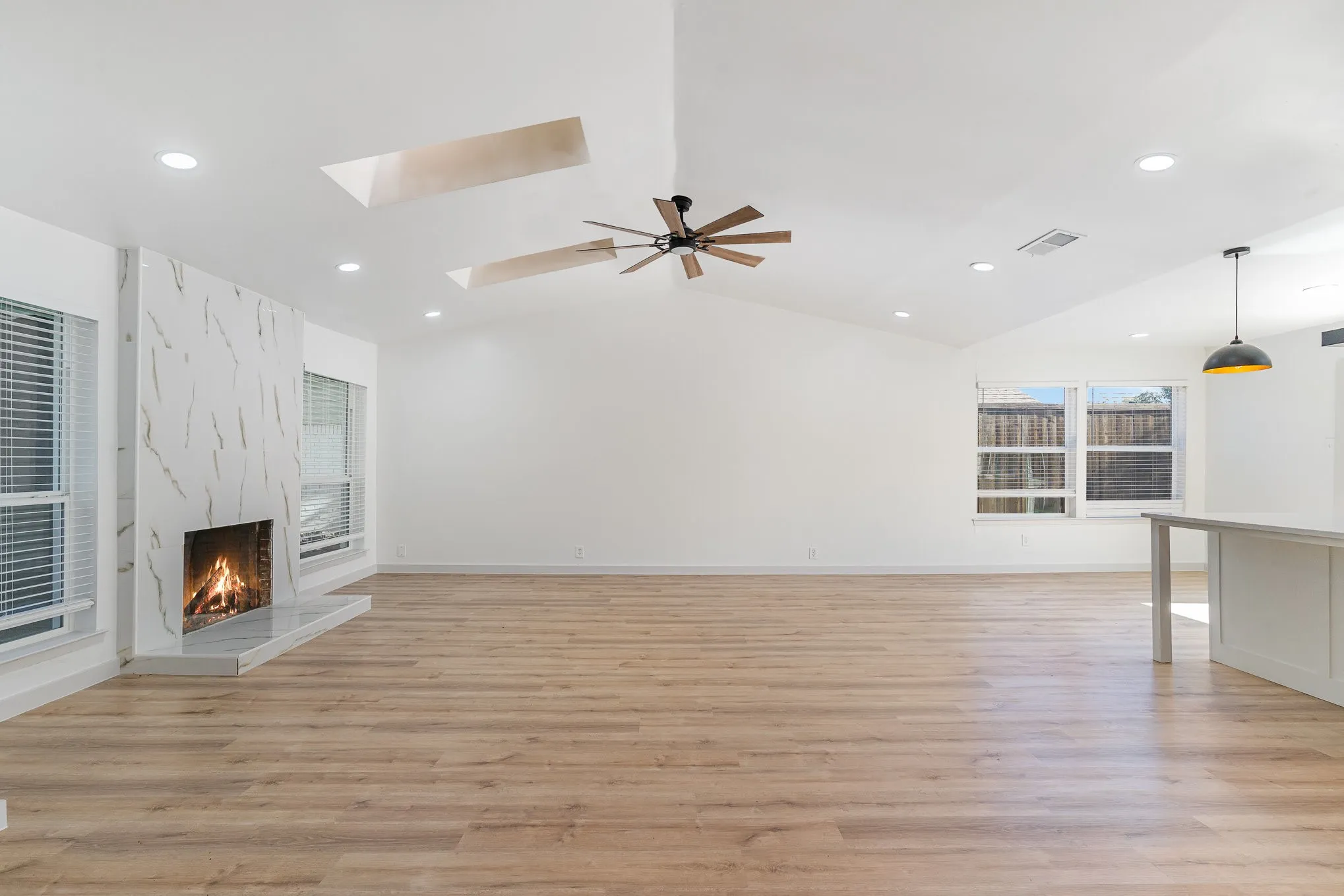 Unfurnished living room featuring a fireplace, ceiling fan, light hardwood / wood-style flooring, and vaulted ceiling with skylight
