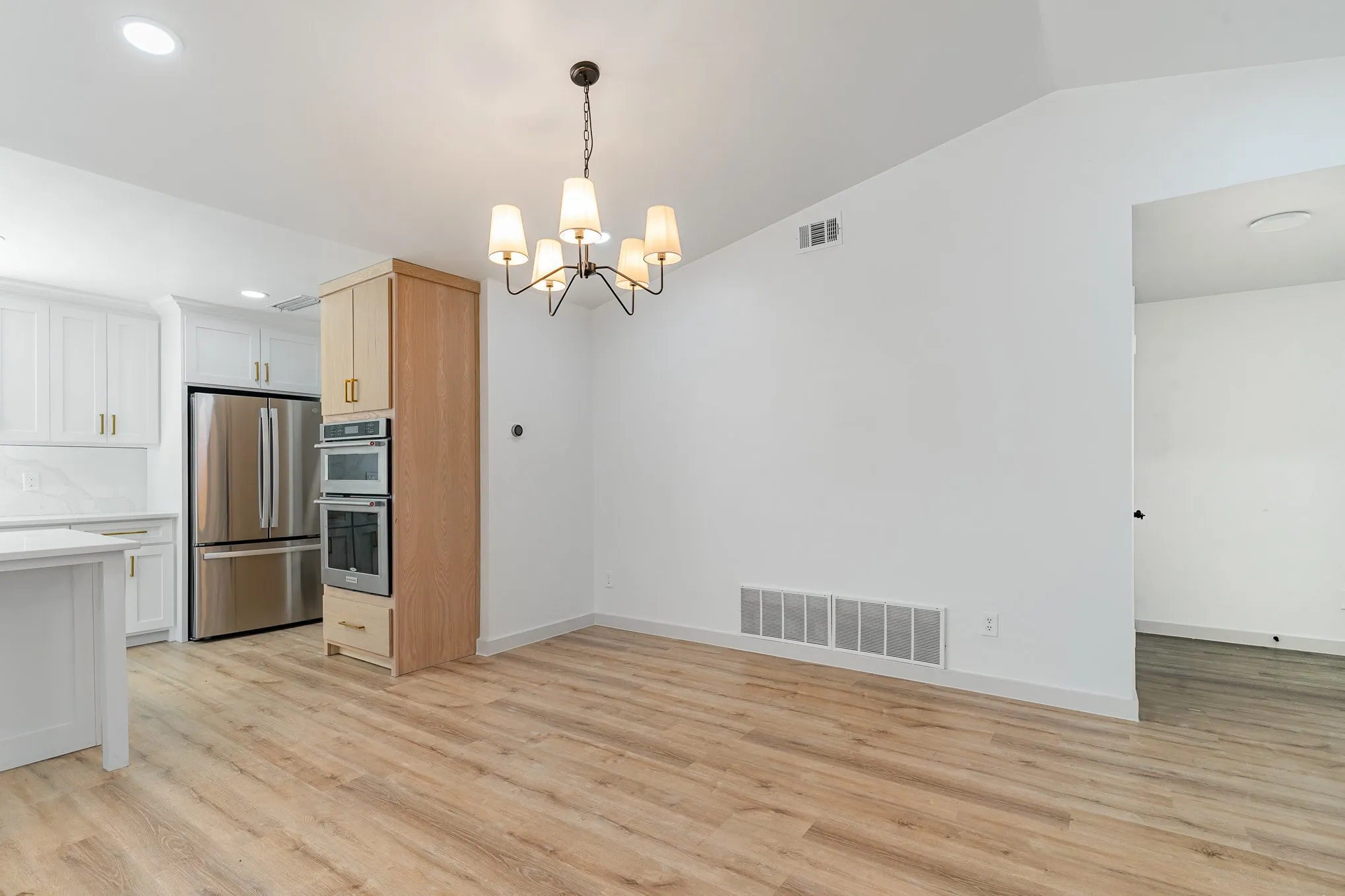 Kitchen with lofted ceiling, white cabinets, light wood-type flooring, stainless steel appliances, and a chandelier