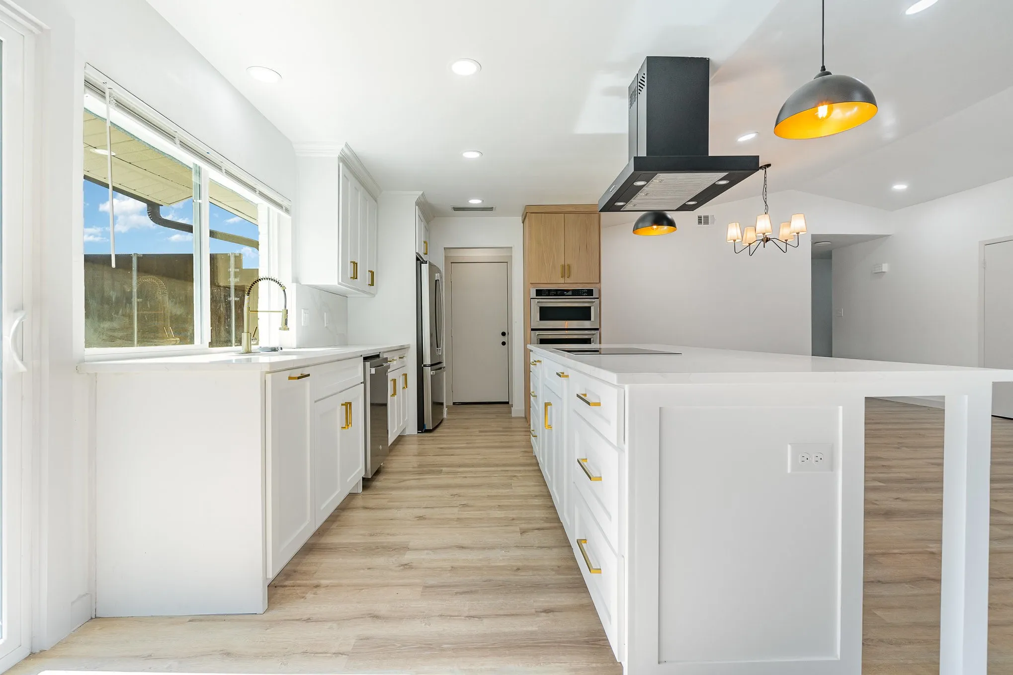 Kitchen with white cabinetry, pendant lighting, range hood, and appliances with stainless steel finishes