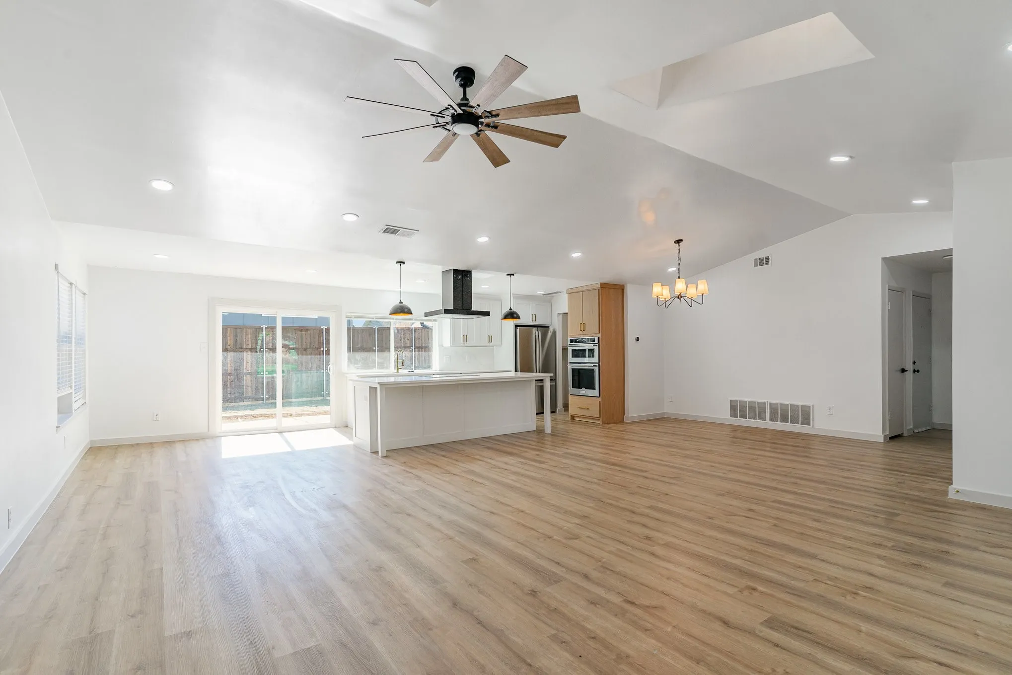 Unfurnished living room with ceiling fan with notable chandelier, light wood-type flooring, and vaulted ceiling