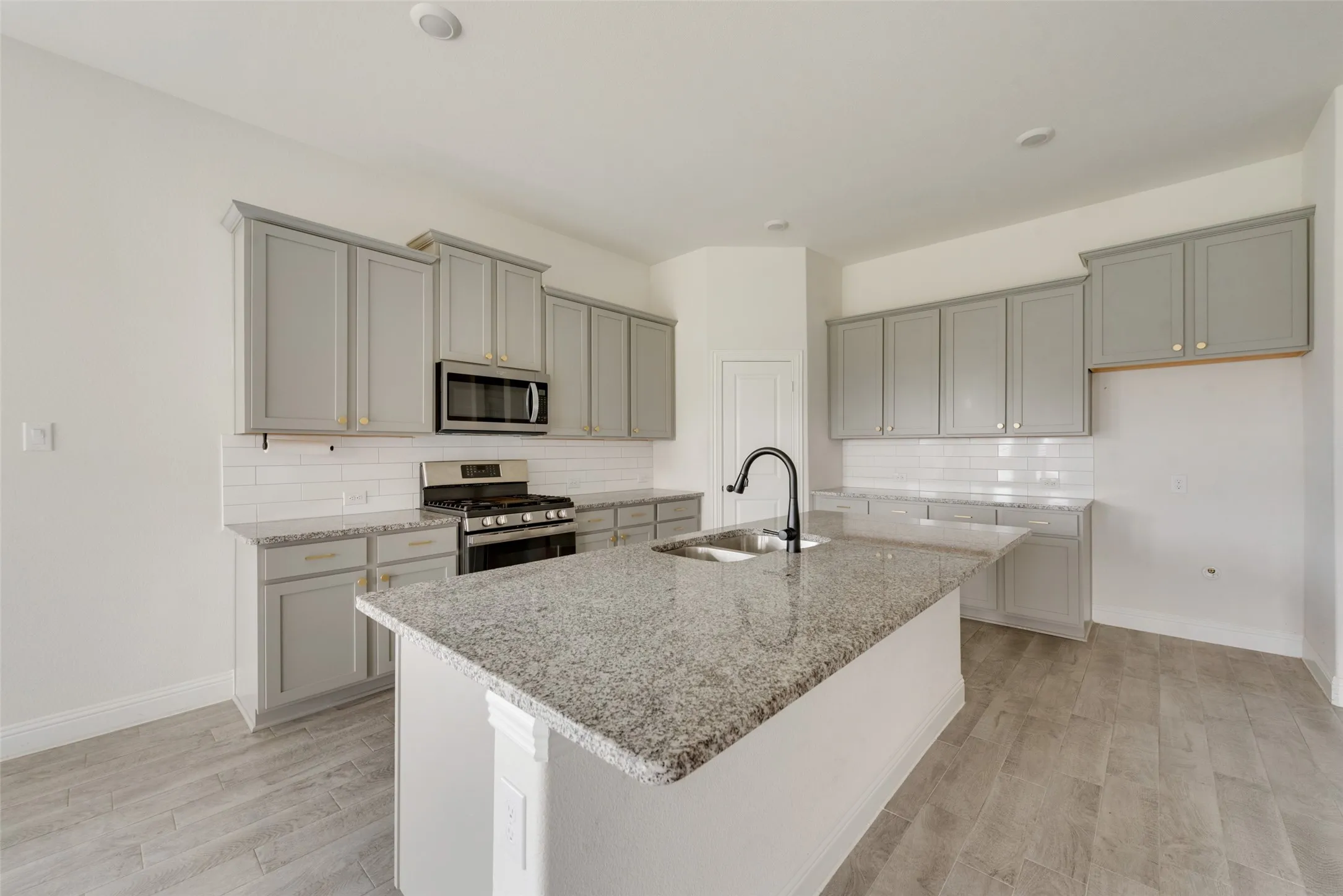 Kitchen with appliances with stainless steel finishes, a kitchen island with sink, light stone counters, sink, and tasteful backsplash