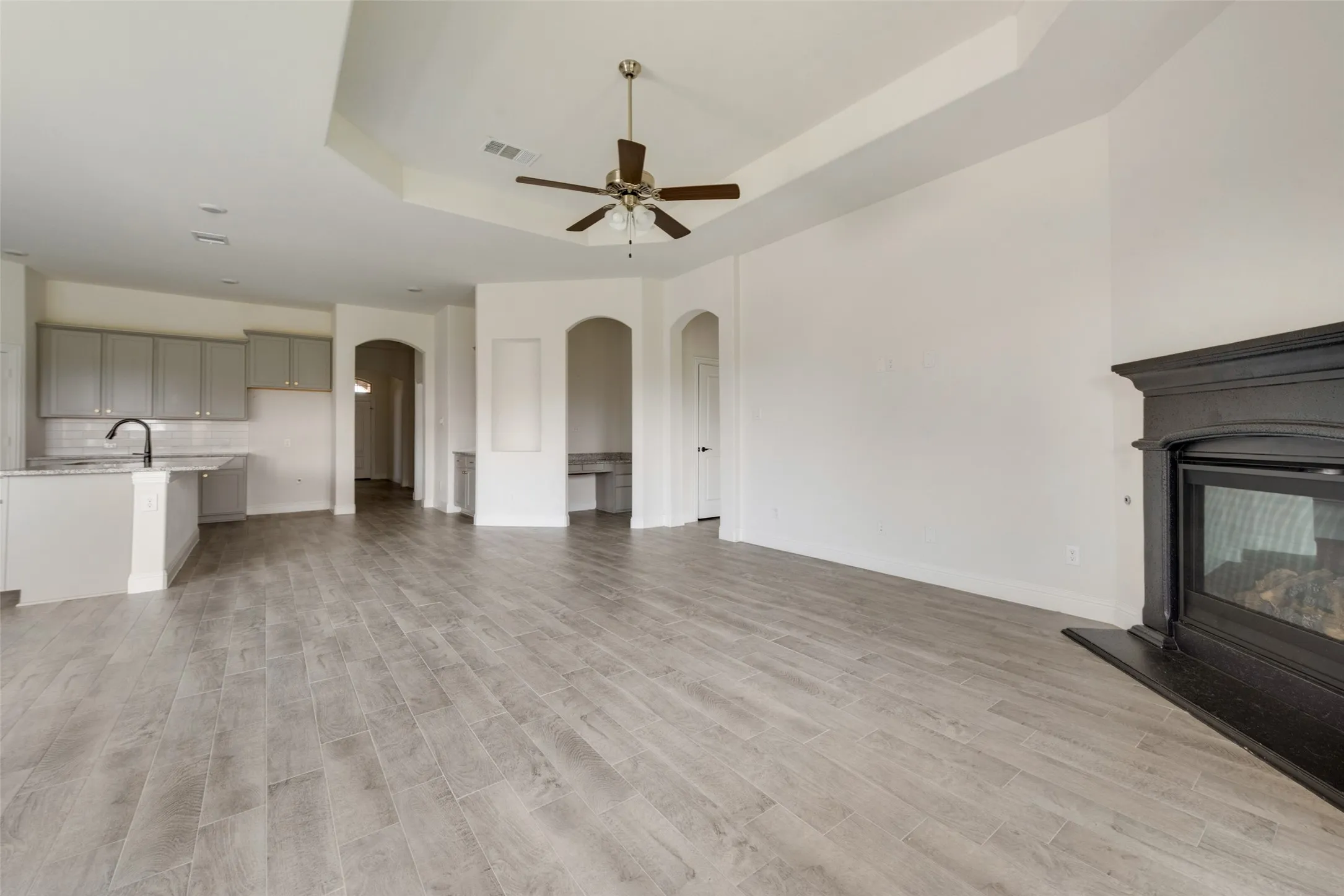 Unfurnished living room featuring ceiling fan, a tray ceiling, light hardwood / wood-style flooring, a multi sided fireplace, and sink