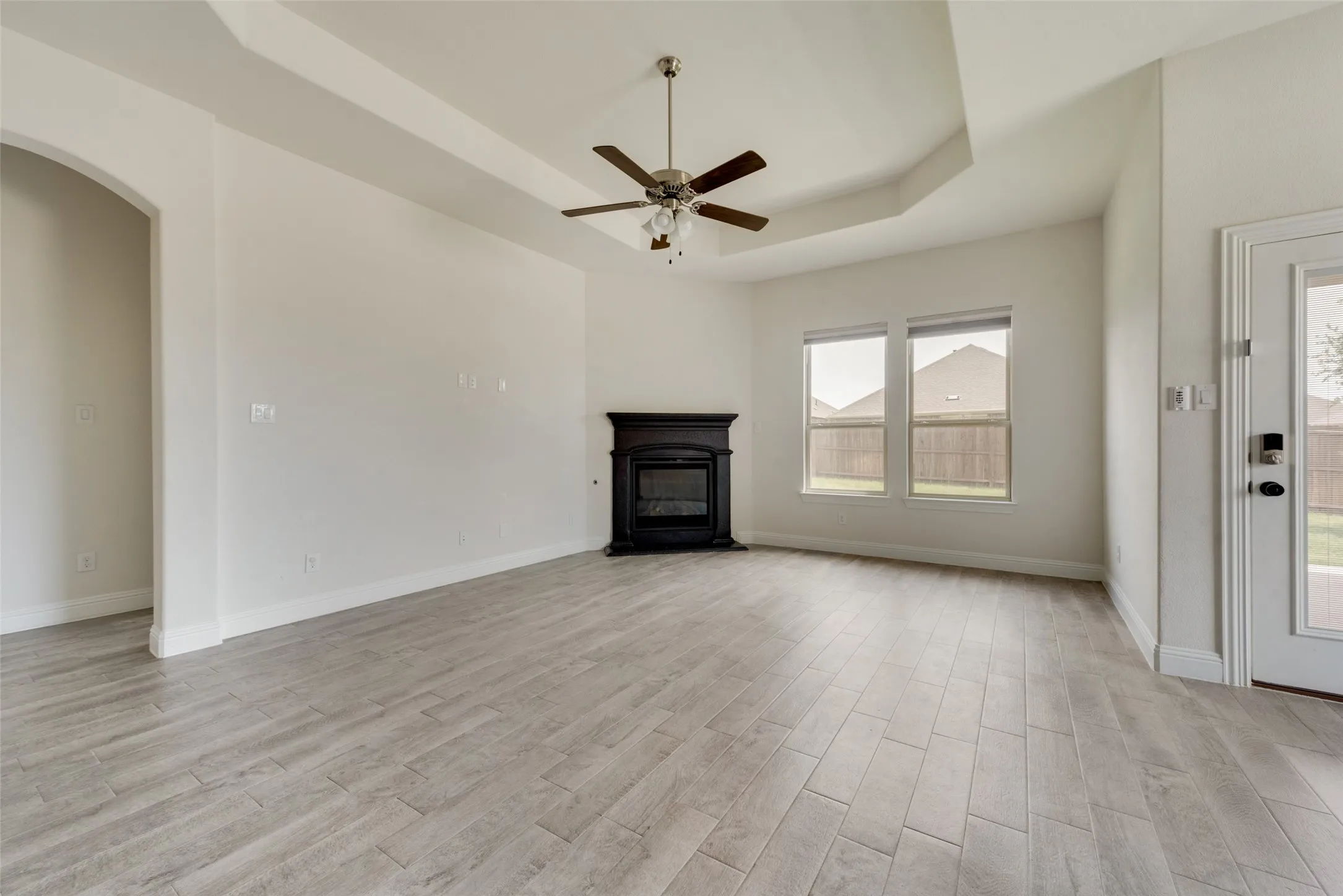 Unfurnished living room featuring a tray ceiling, light wood-type flooring, and ceiling fan