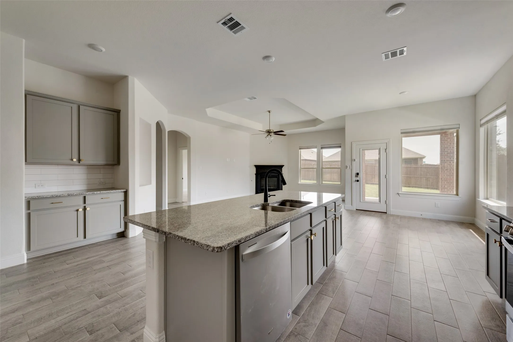 Kitchen with light hardwood / wood-style floors, stone counters, a kitchen island with sink, stainless steel dishwasher, and sink