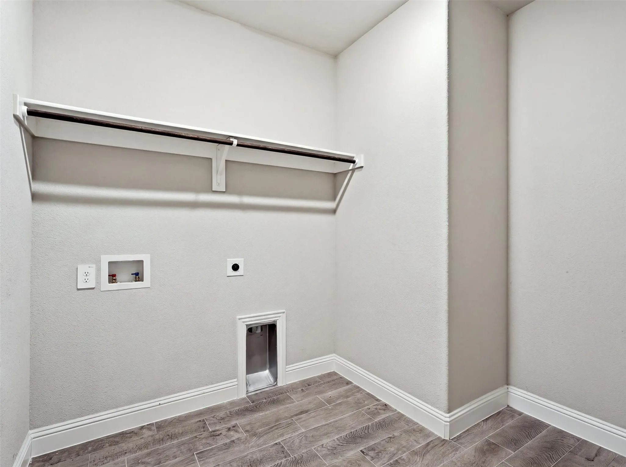 Dedicated laundry space featuring wood-finish flooring, built-in shelving, and a clothing rod