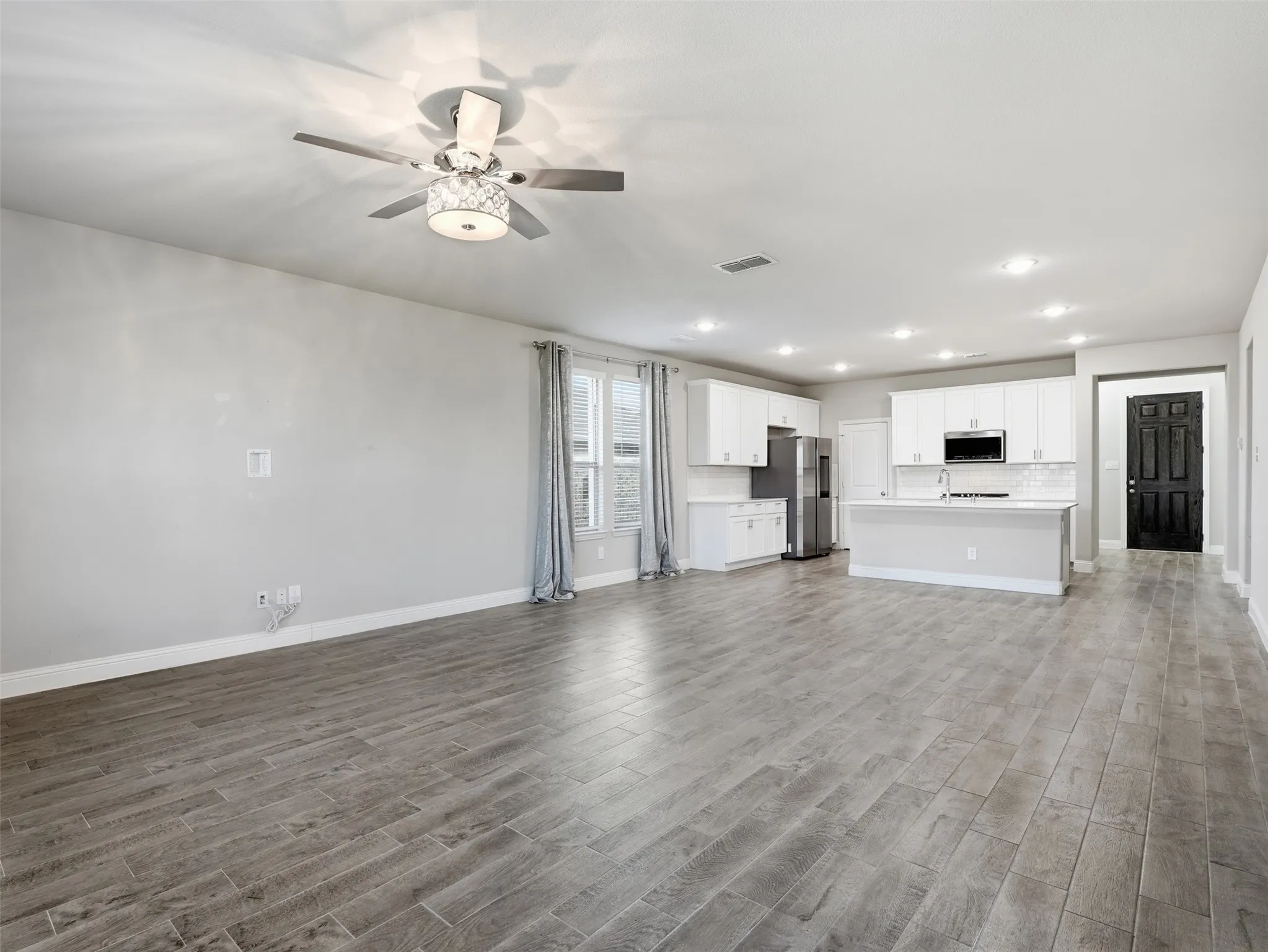 Open-concept living space featuring wood-finish flooring, recessed lighting, a ceiling fan, white cabinetry, and stainless steel appliances
