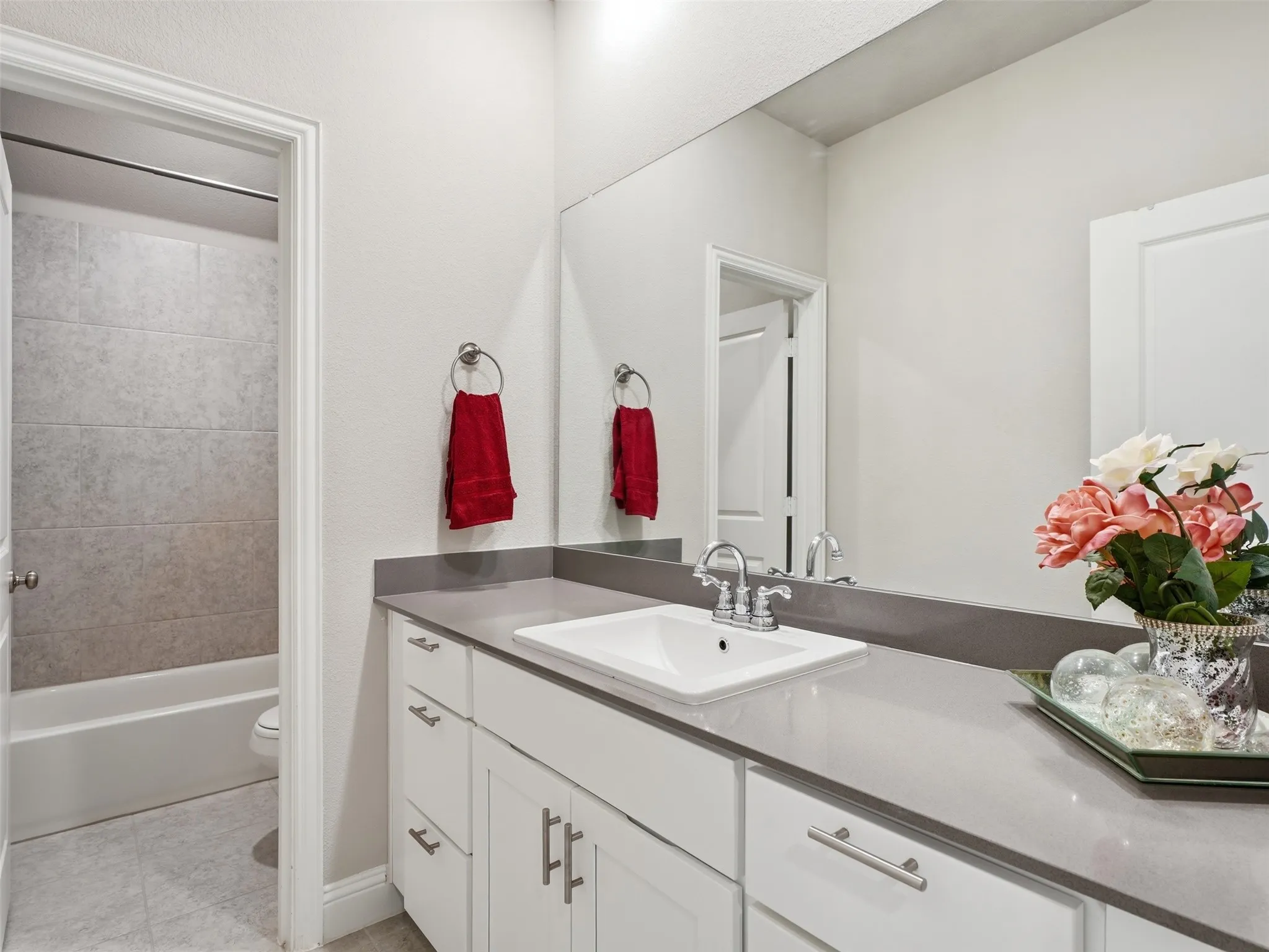 Bathroom featuring a vanity with an integrated sink, polished chrome faucet, stone-finish countertop, white cabinetry with brushed nickel hardware, and an adjacent full-size bathtub with tiled surround